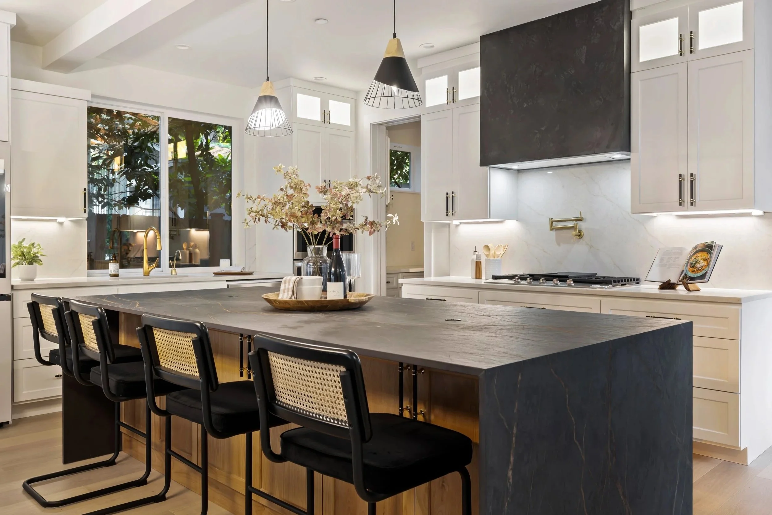 Kitchen island with dark Dekton countertop with copper veining, white cabinetry, modern pendant lights and brass and marble accents.