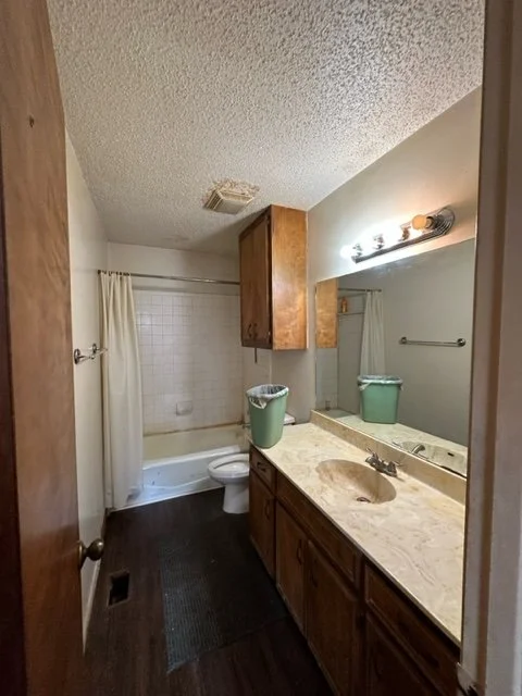 Bathroom before renovation with original dated vanity and cabinet, popcorn ceiling and older fixtures.