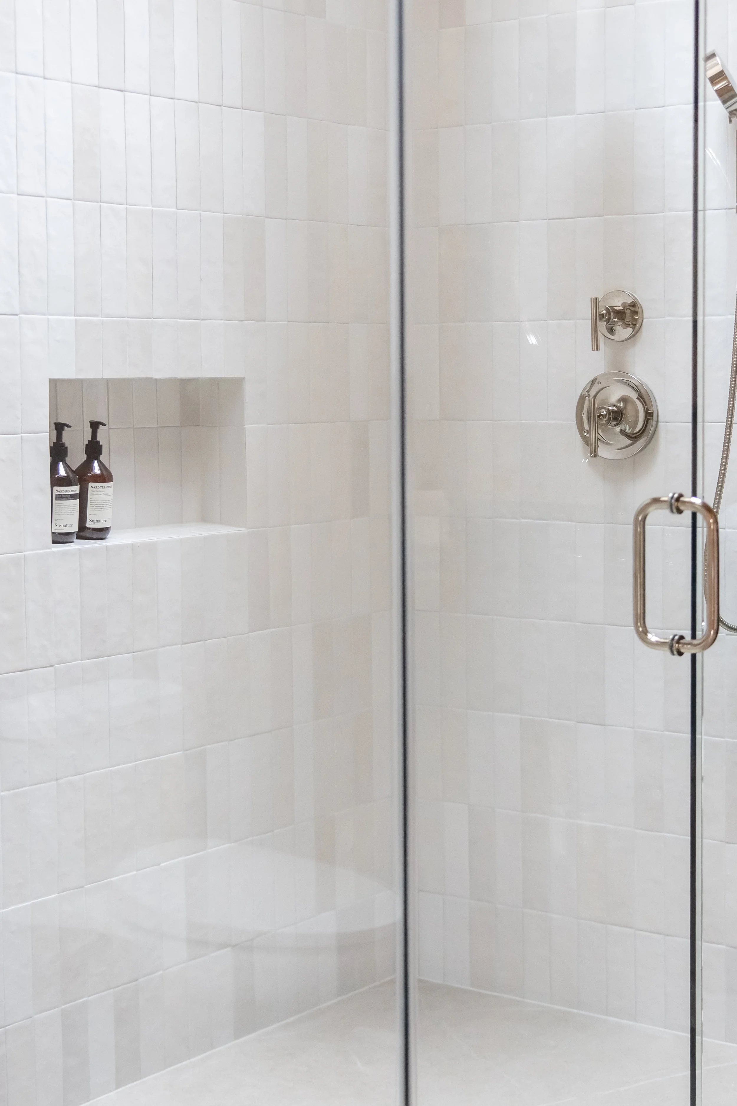 Guest bathroom shower with white zellige-style tile, glass enclosure, shower niche and polished nickel fixtures.