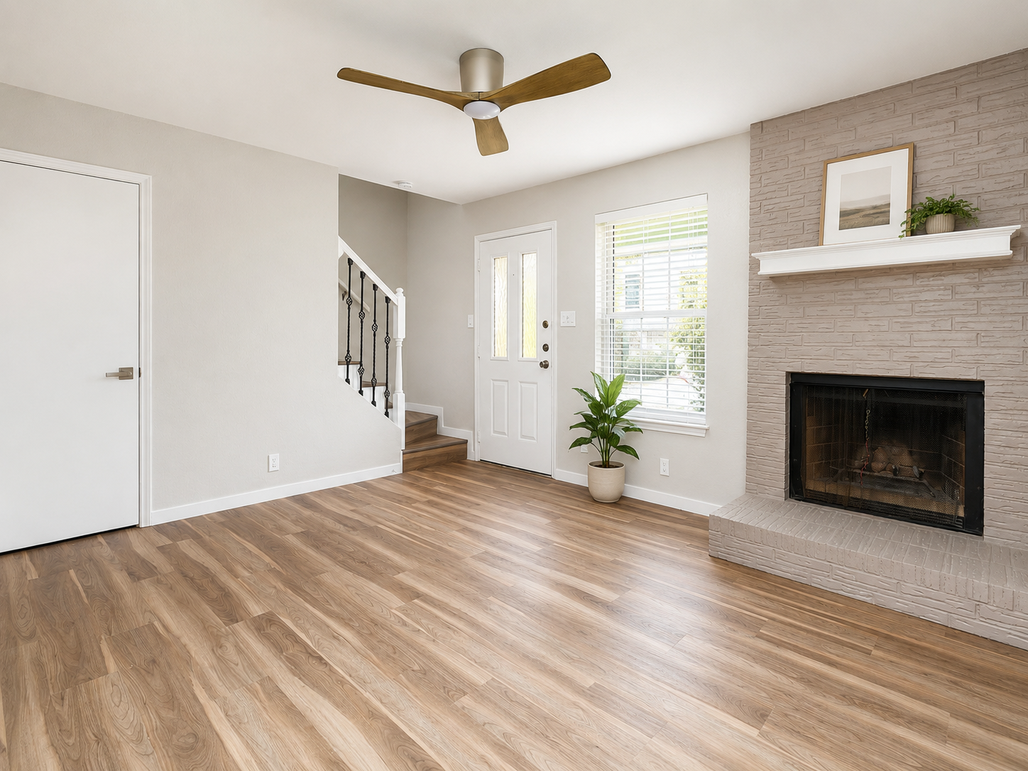 Living room with neutral painted fireplace, LVP flooring, modern wood ceiling fan and neutral walls.