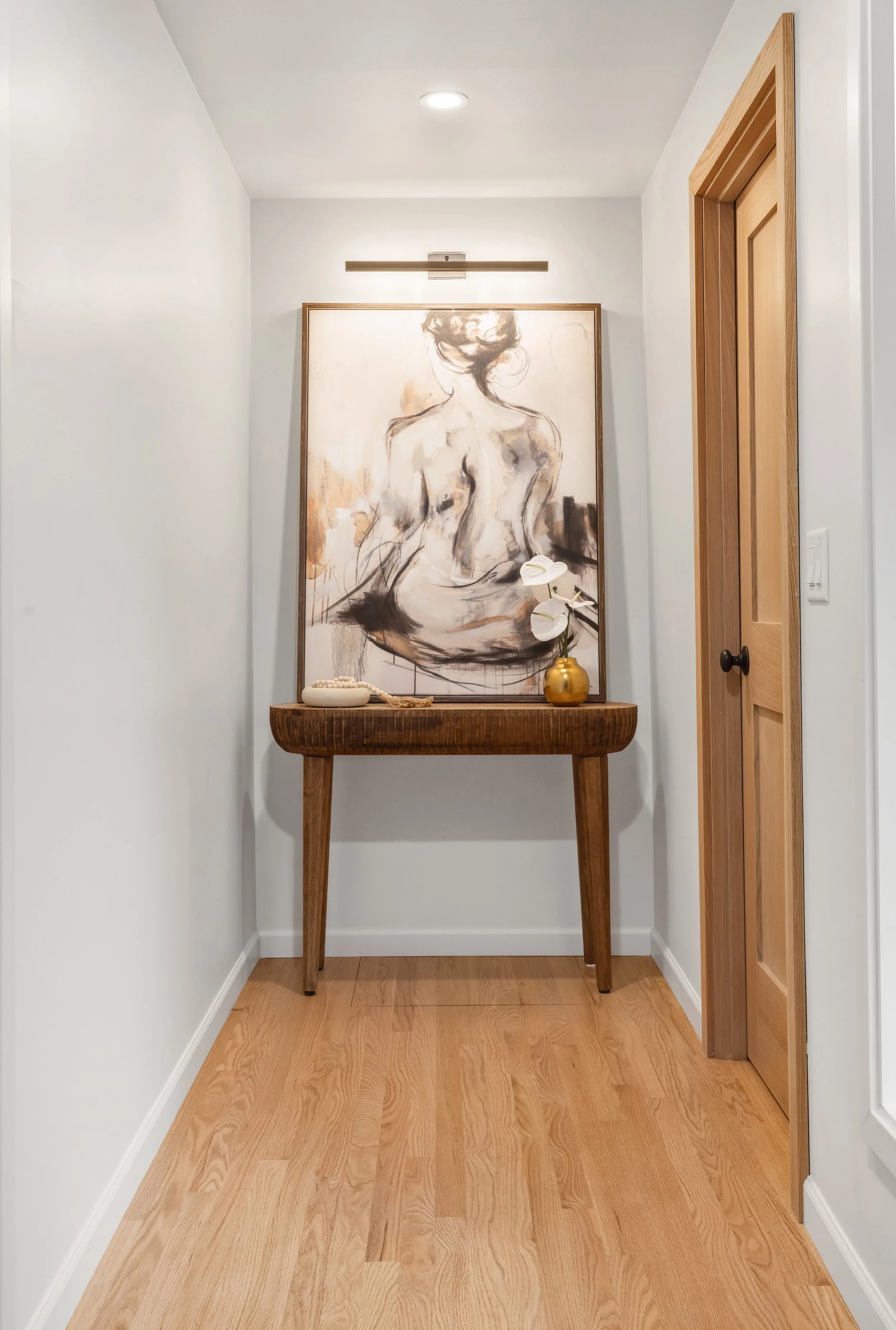 Hallway with natural wood floors and doors, and accent lighting highlighting artwork.