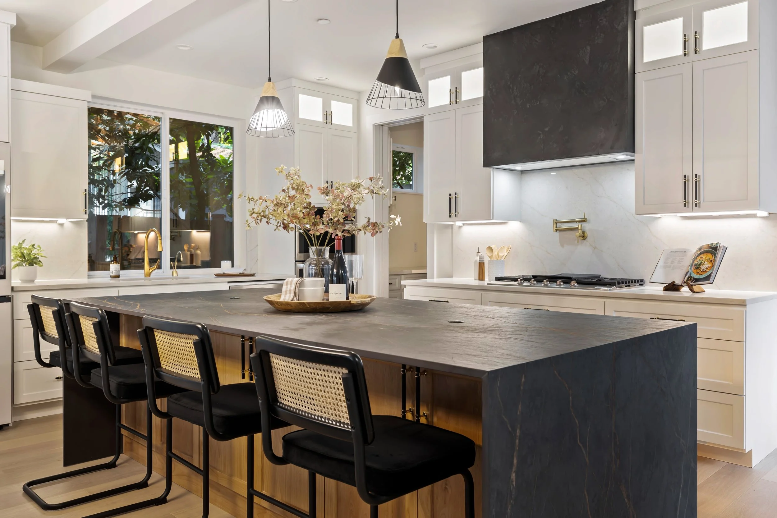 Modern kitchen design featuring white cabinetry, black marble island, and brass fixtures creating strong contrast and contemporary aesthetic.