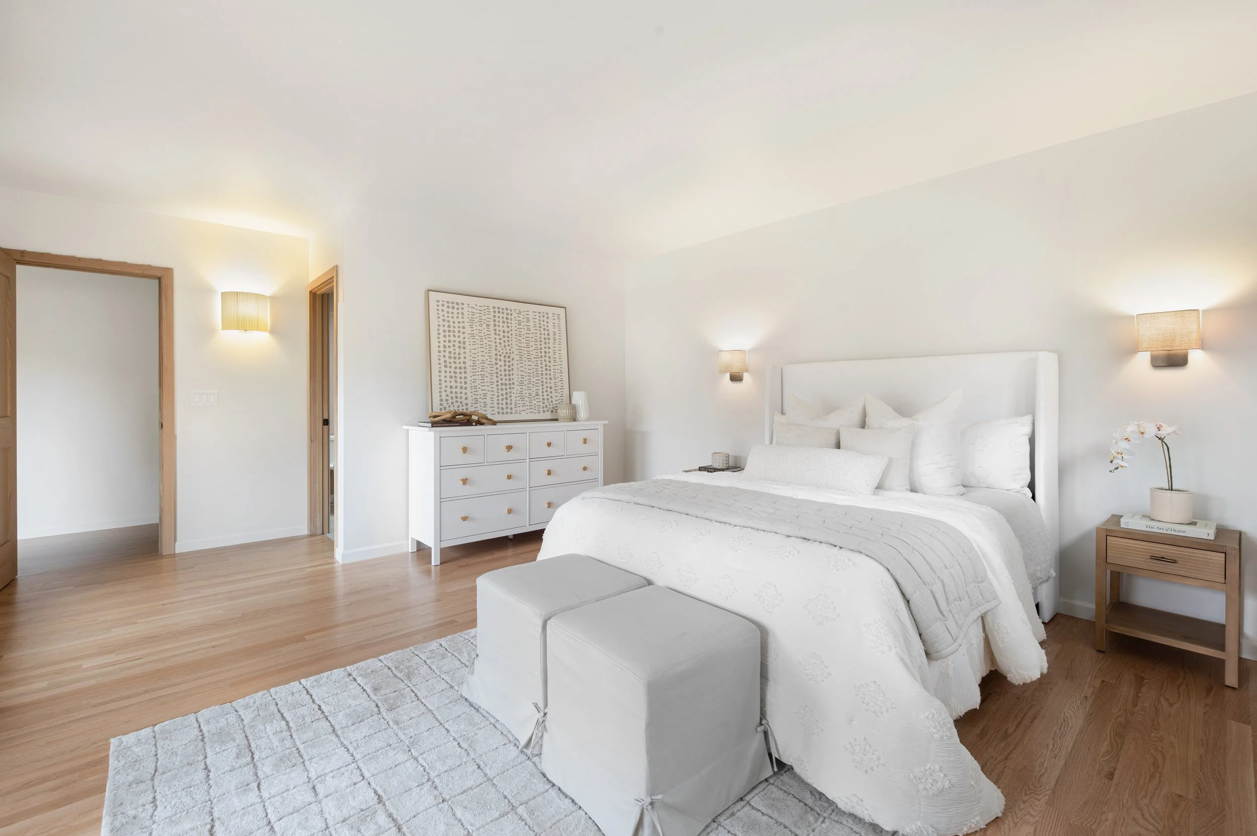 Guest bedroom with white bedding, natural wood flooring, linen wall sconces and soft neutral palette.