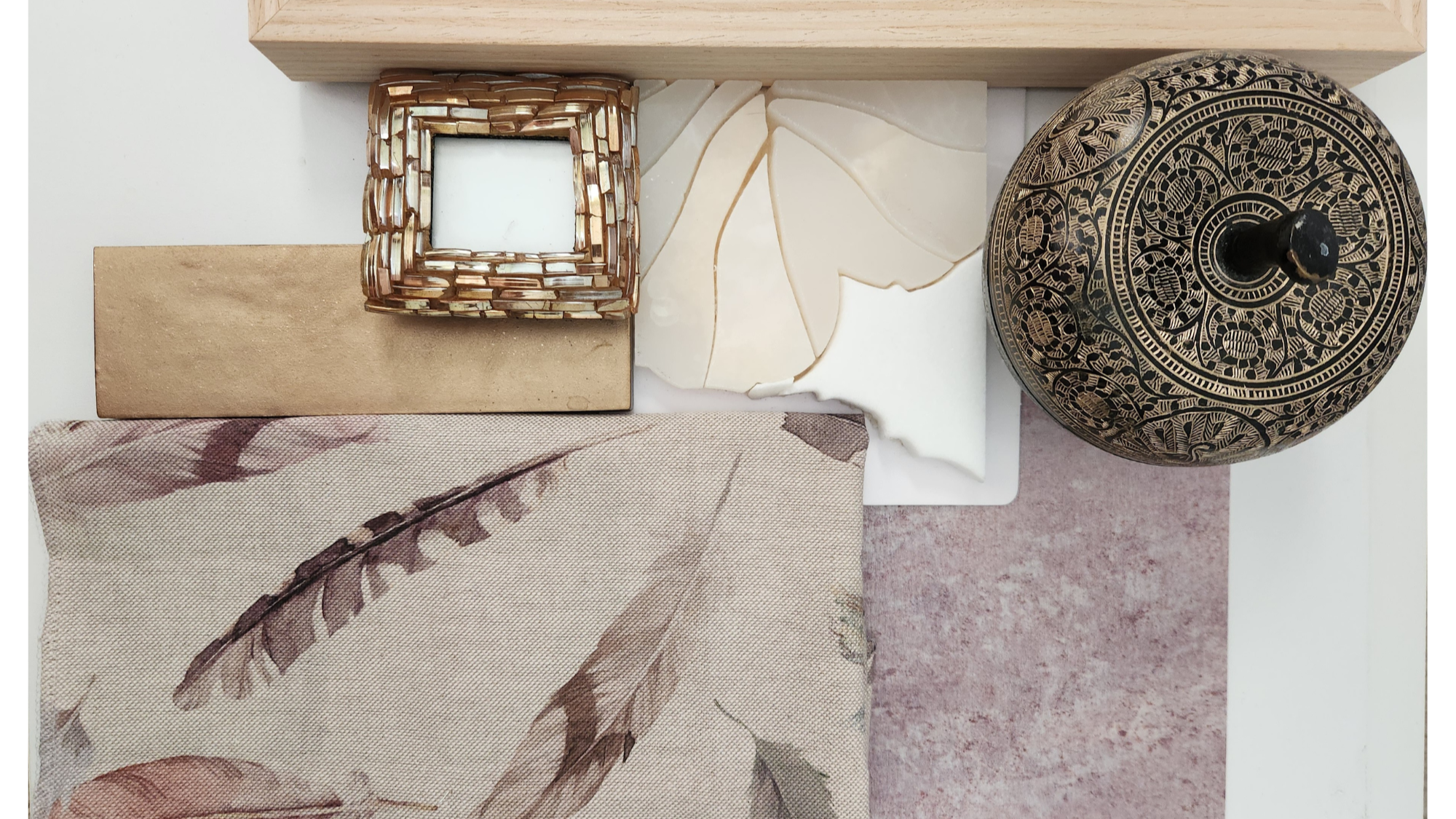 Overhead view of mixed materials and textures—patterned fabric with feather motifs, metallic purple wallpaper, natural wood, golden glass frame, waterjet stone mosaic tile, golden ceramic tile and brass and black etched box.