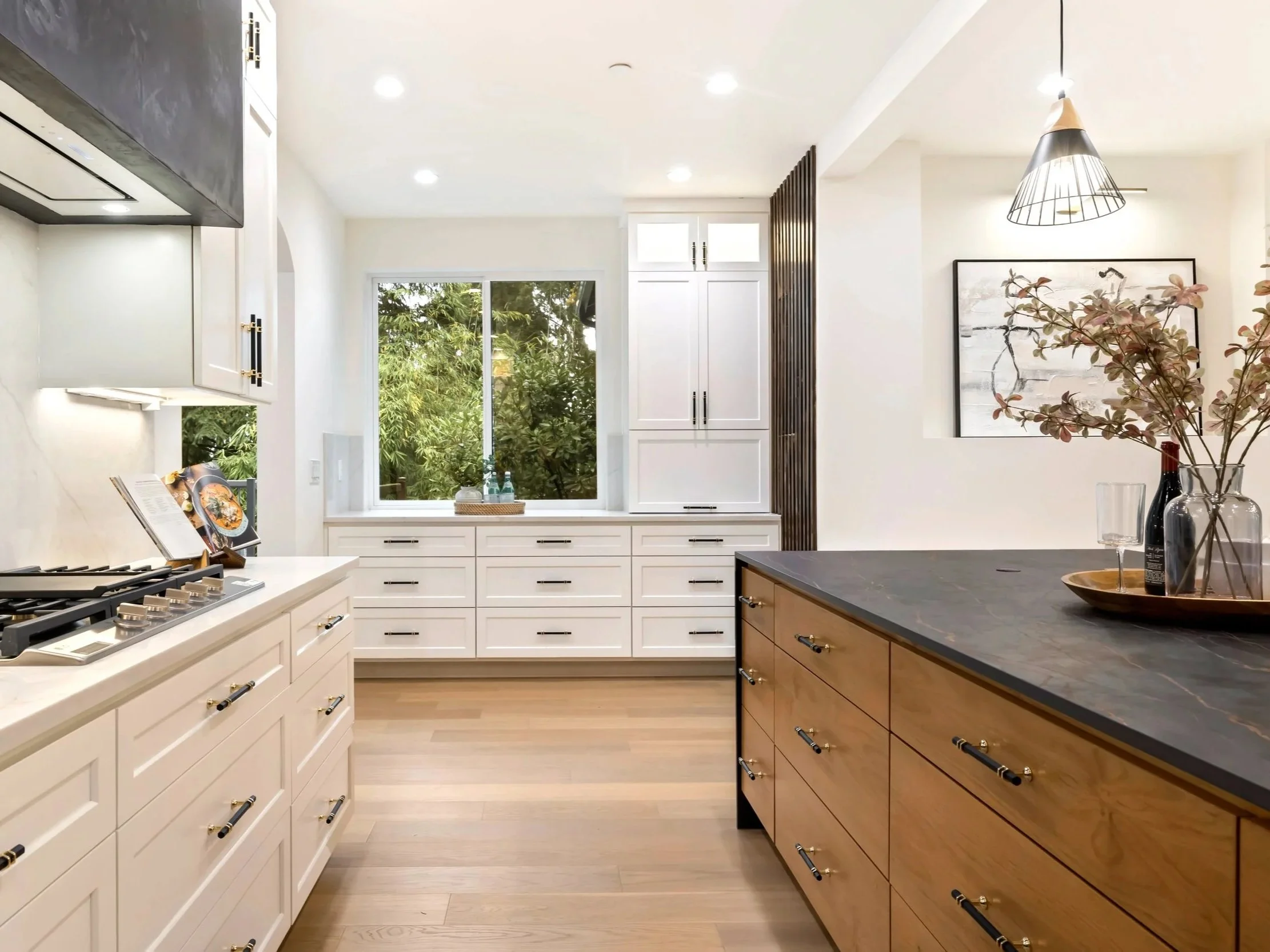 Kitchen with white cabinetry, dark countertops with copper veining, stainless steel cooktop, black plaster hood and brass and marble hardware.