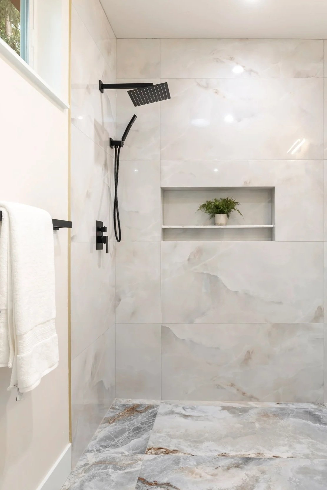 Secondary bathroom with marble-look porcelain tile in curbless shower and integrated shelving.