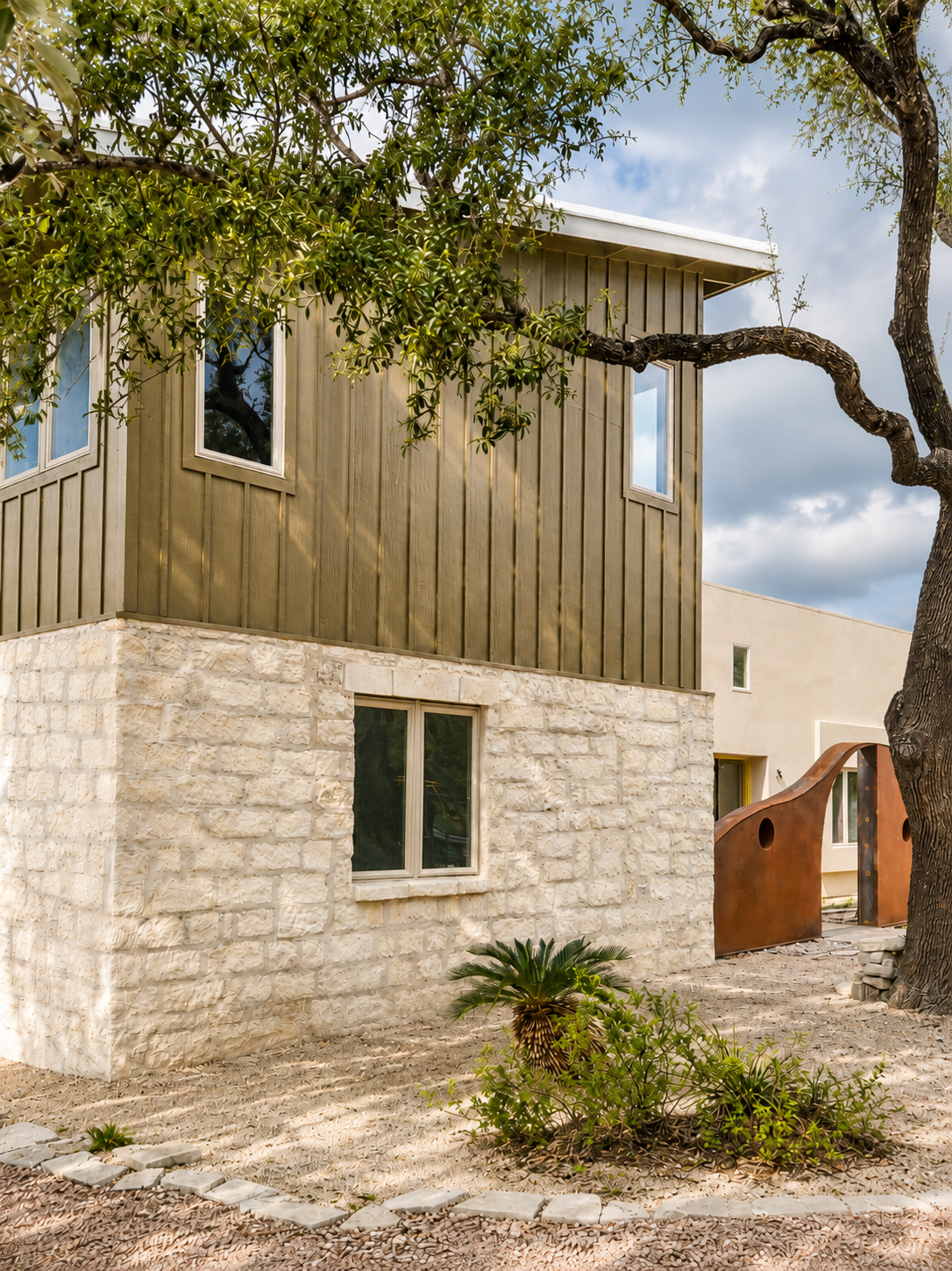 Modern home exterior with painted board and batten, limestone, beige stucco, large windows, native landscaping, and a custom wall with gate.