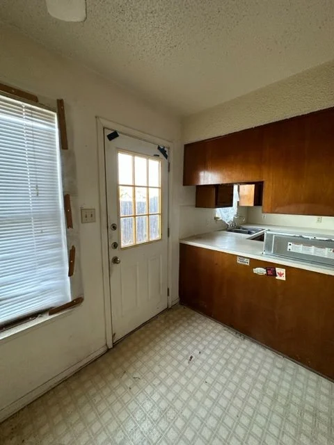 Kitchen before renovation with original dark wood cabinetry enclosing the kitchen, vinyl flooring and popcorn ceiling.