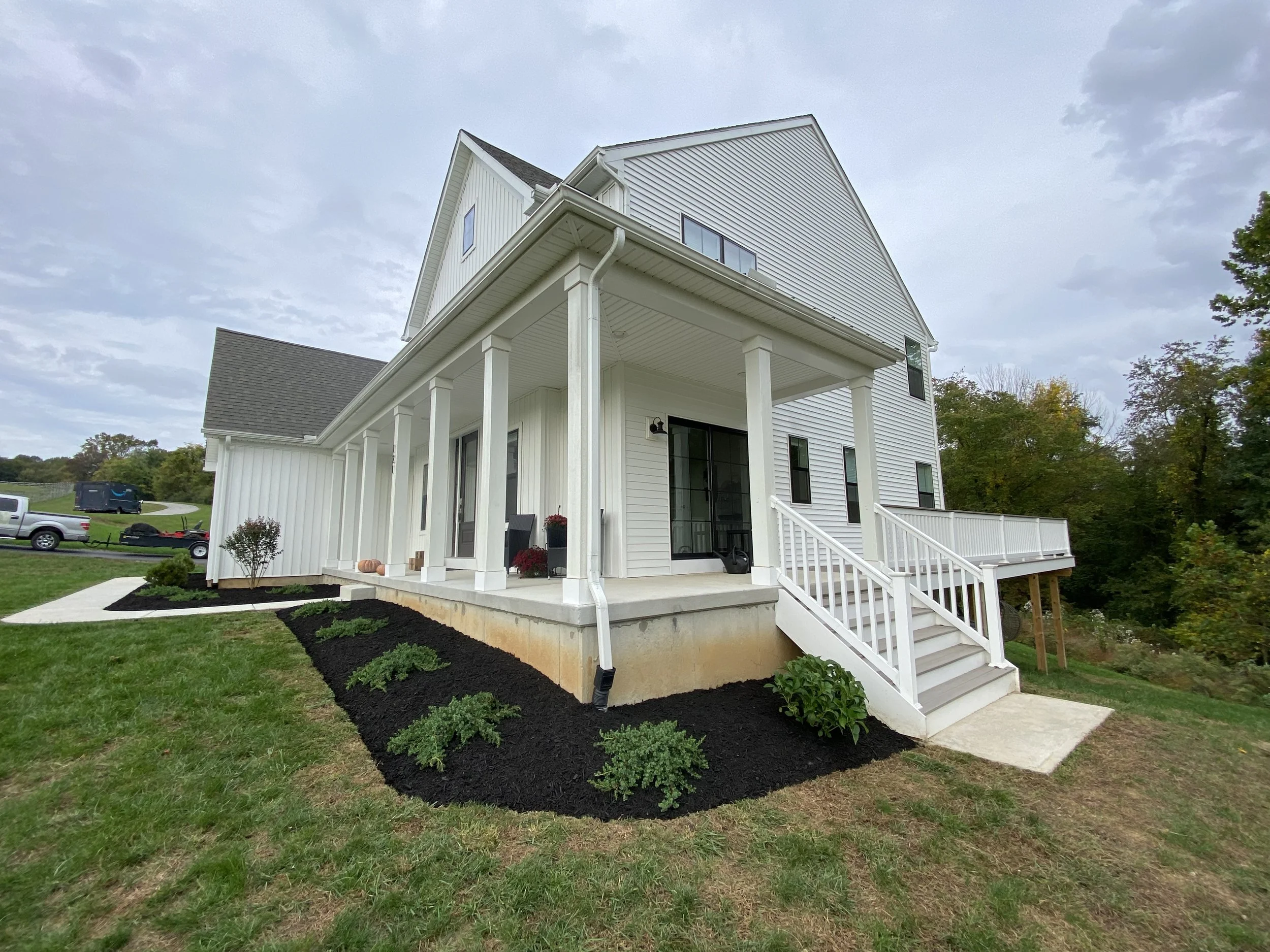 Front view of a white modern house with a covered porch, small stairs, well-maintained garden, and lawn, with a partly cloudy sky.