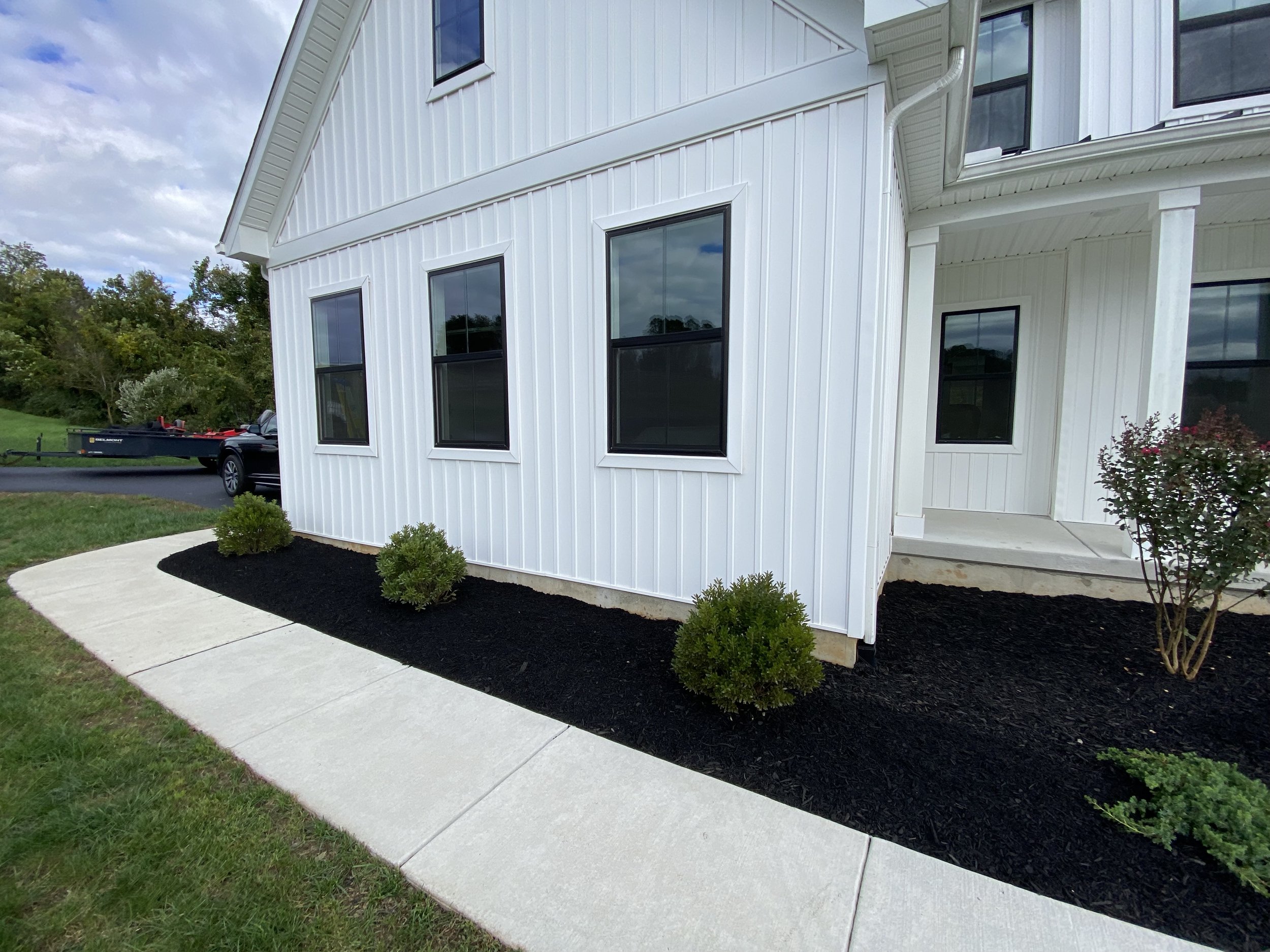 Modern white house with black window frames, small bushes, and a curved concrete walkway.