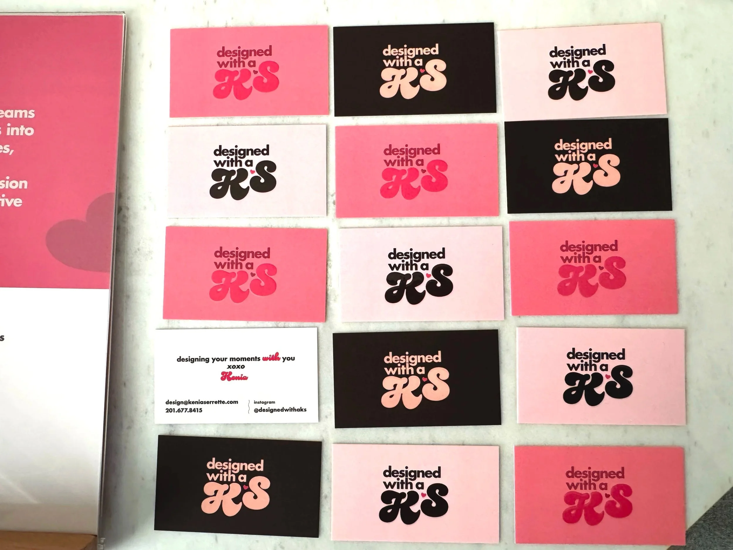 Array of 14 business cards with pink, black, white, and pink backgrounds, each displaying the phrase "designed with a KS" and a small hearts. One card has additional text with contact information and social media handle.