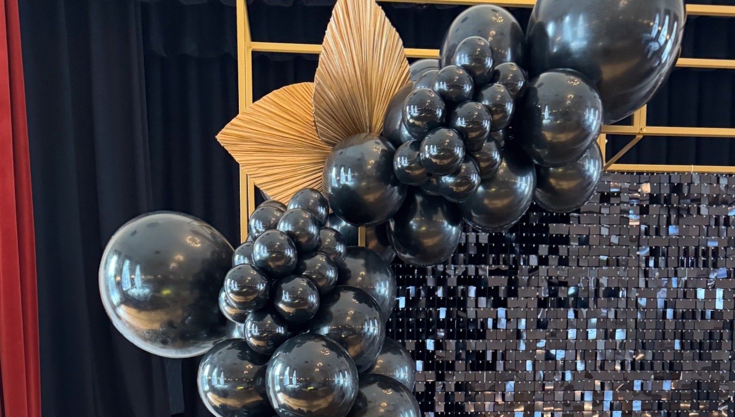 Black balloons arranged with metallic gold leaves and a black mosaic backdrop