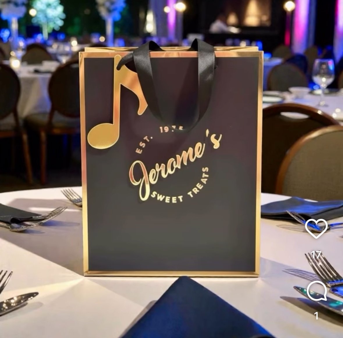 A gift bag from Jeriame's Sweet Treats placed on a dining table, with silverware and napkins, in a decorated banquet hall with colorful lighting.