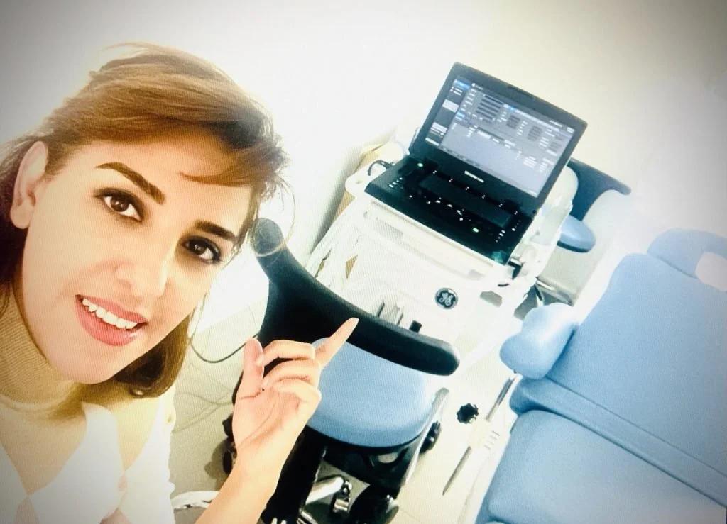 A woman in a medical setting pointing at a computer screen on a hospital bed.