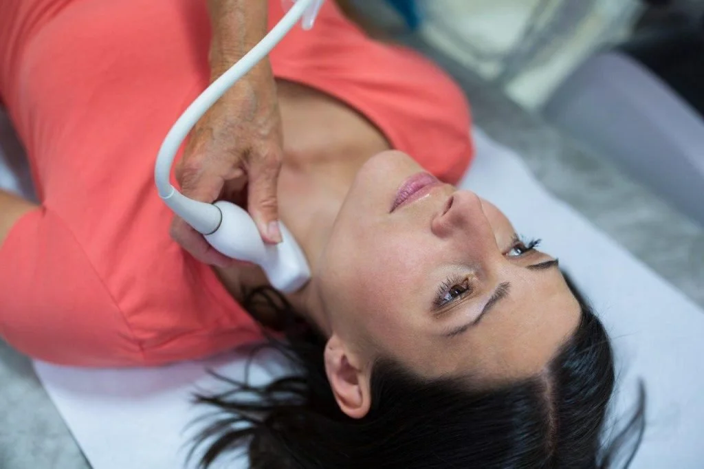 A woman lying on an examination table receiving an ultrasound scan on her neck.