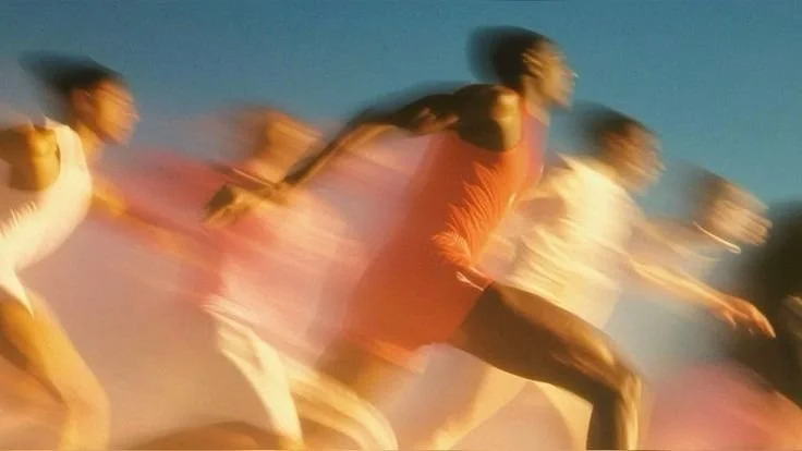 Motion-blurred group of runners training outdoors under a blue sky, representing speed, endurance, and active running lifestyles.