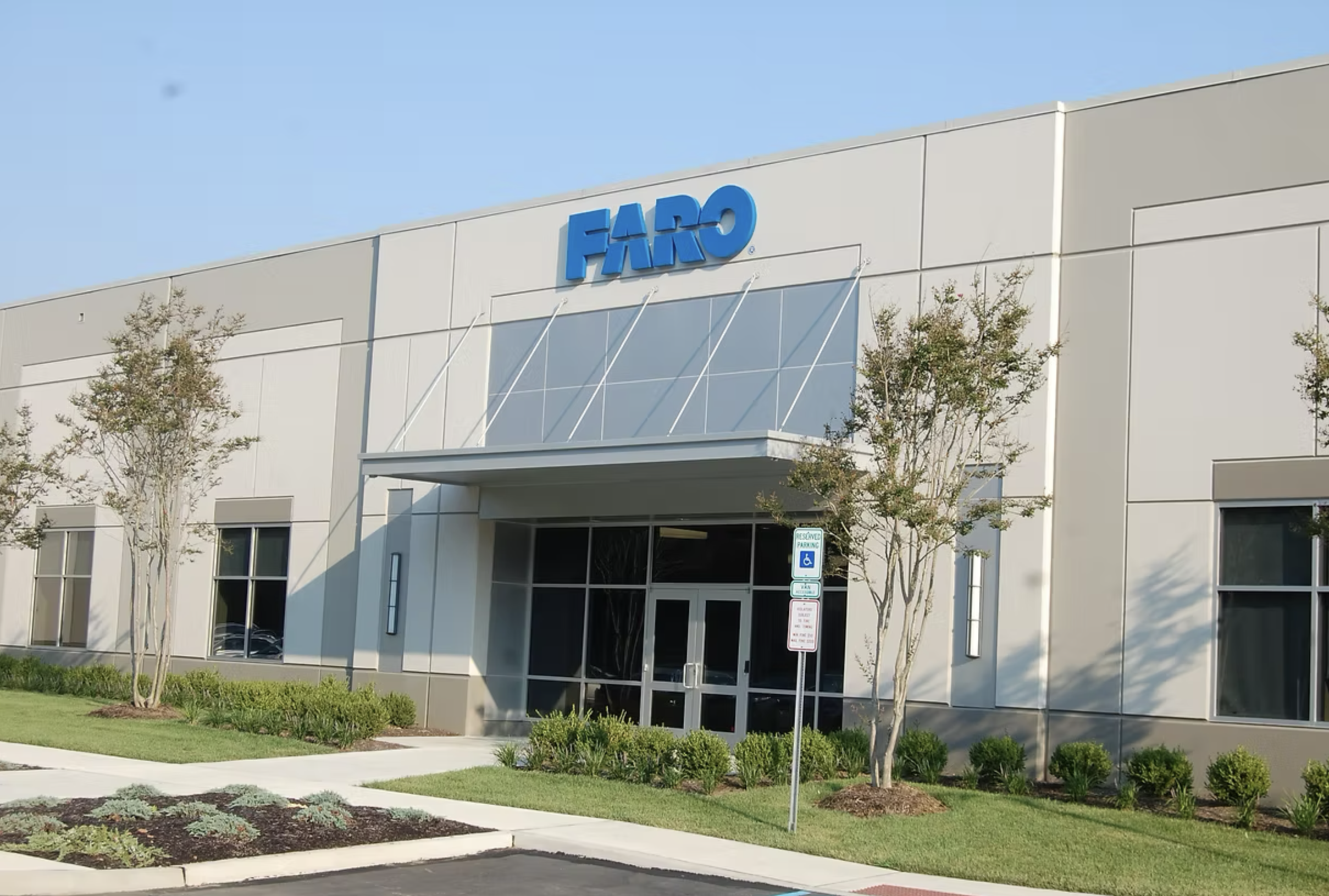 Exterior of a large warehouse-style building with a blue FARRO sign, glass entrance doors, small trees, and manicured bushes in front, with a sunny sky.
