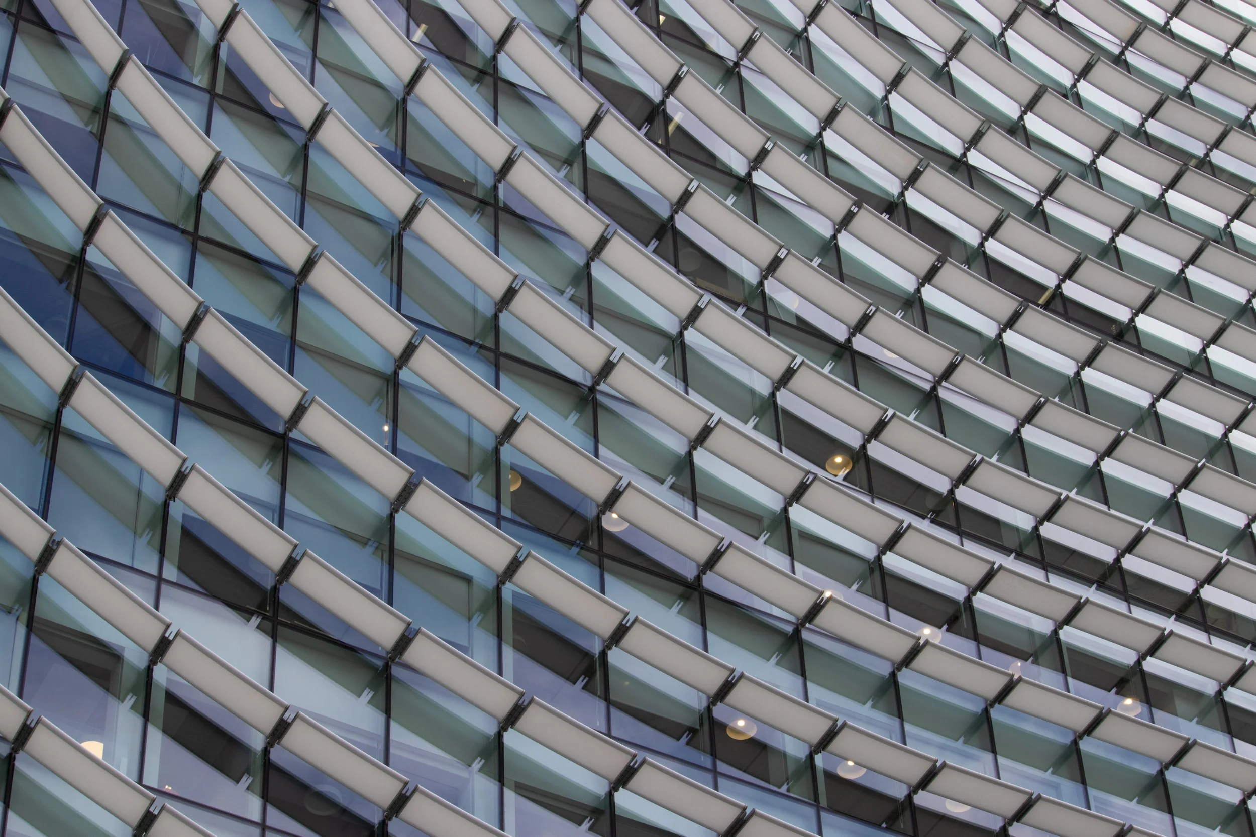 Close-up view of a modern building's glass facade with white structural supports creating a geometric pattern.