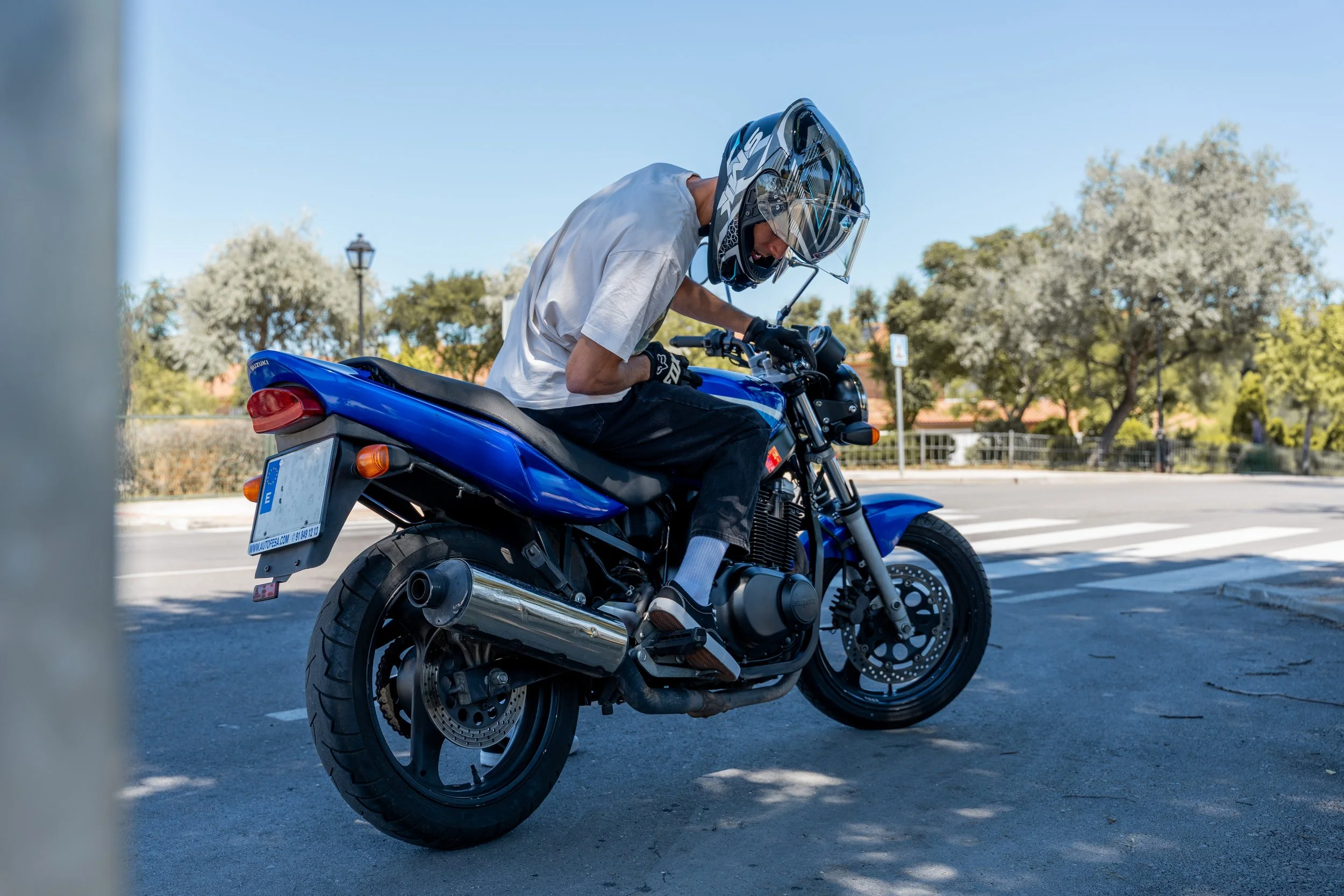 A man wearing a helmet and gloves riding a blue motorcycle on a sunny day