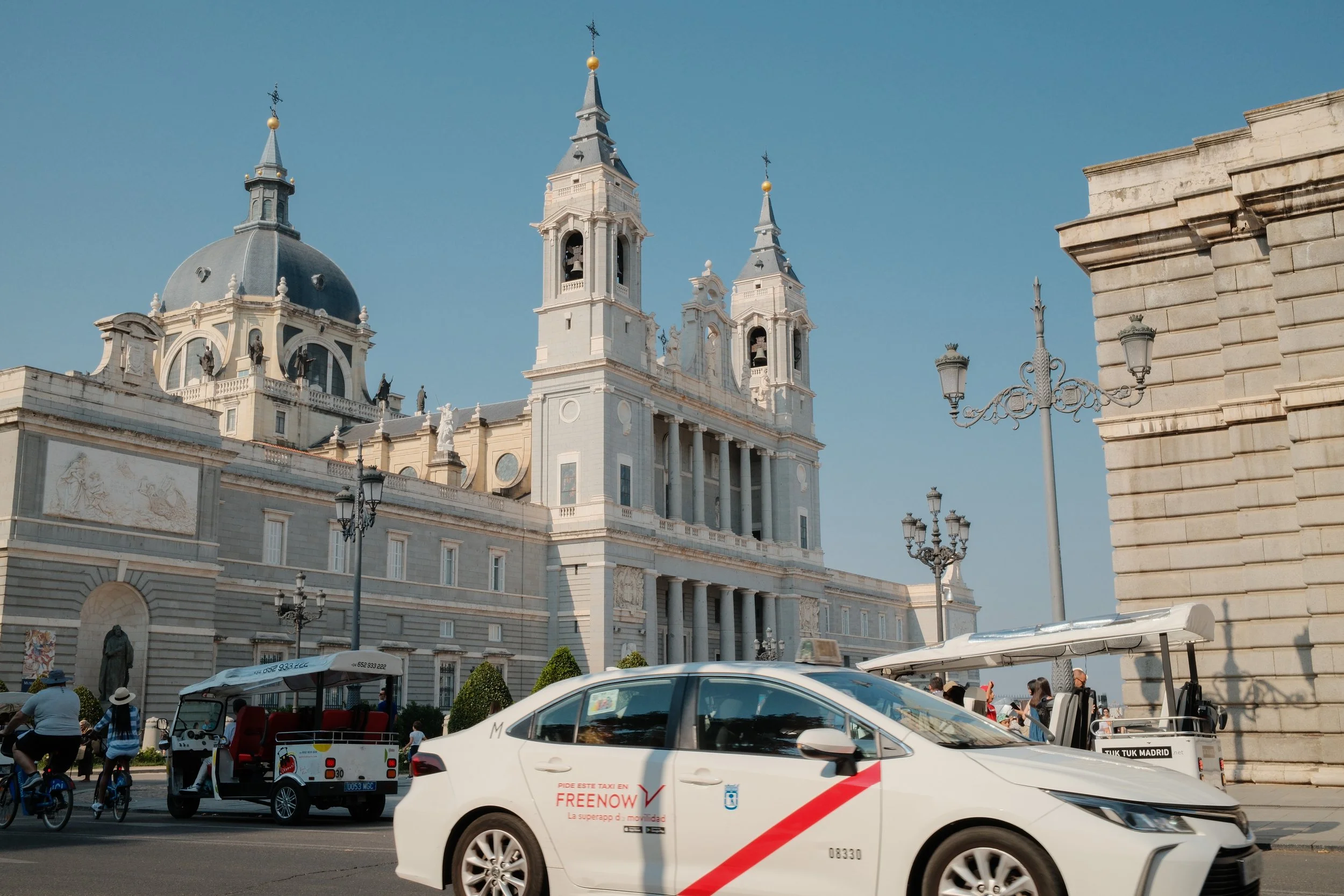 Street scene in Madrid with taxis, cyclists, and a historic church in the background.