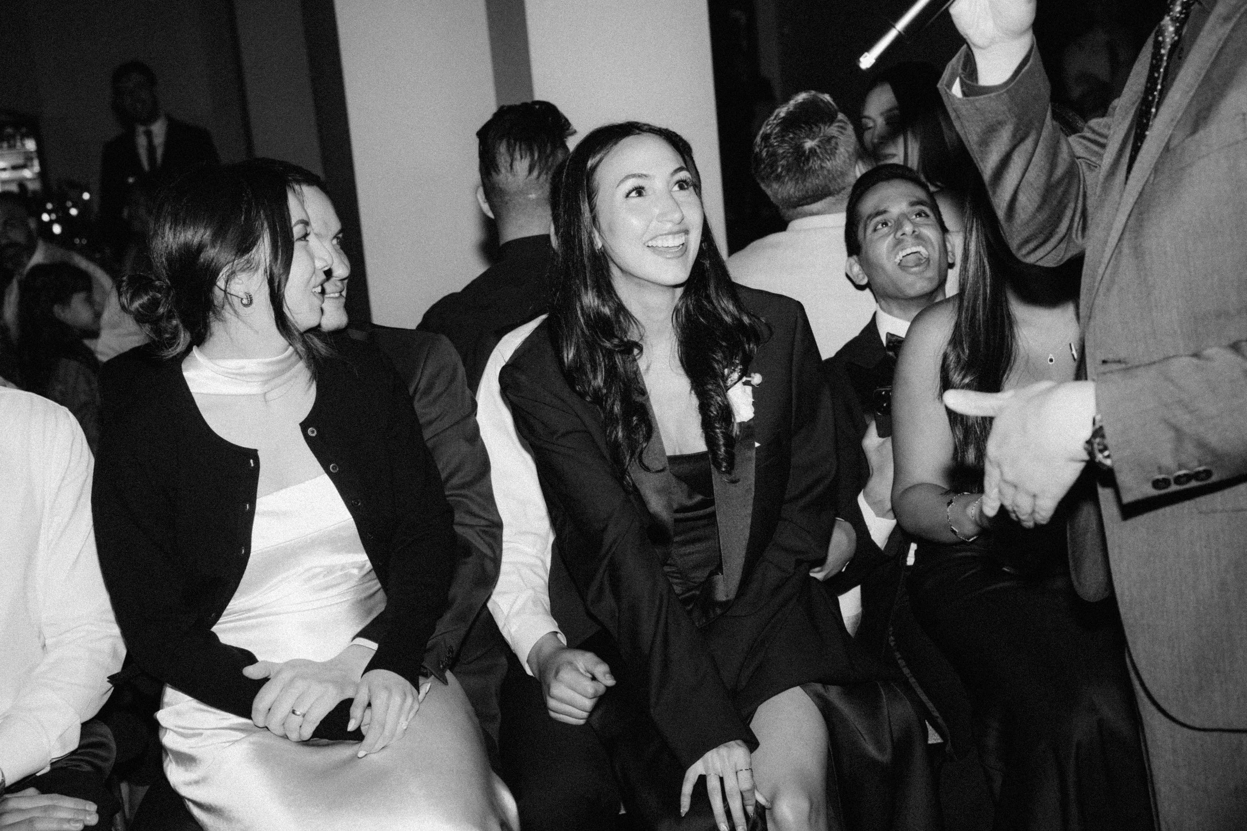 Group of people sitting at a formal event, smiling and engaging with a speaker holding a microphone.