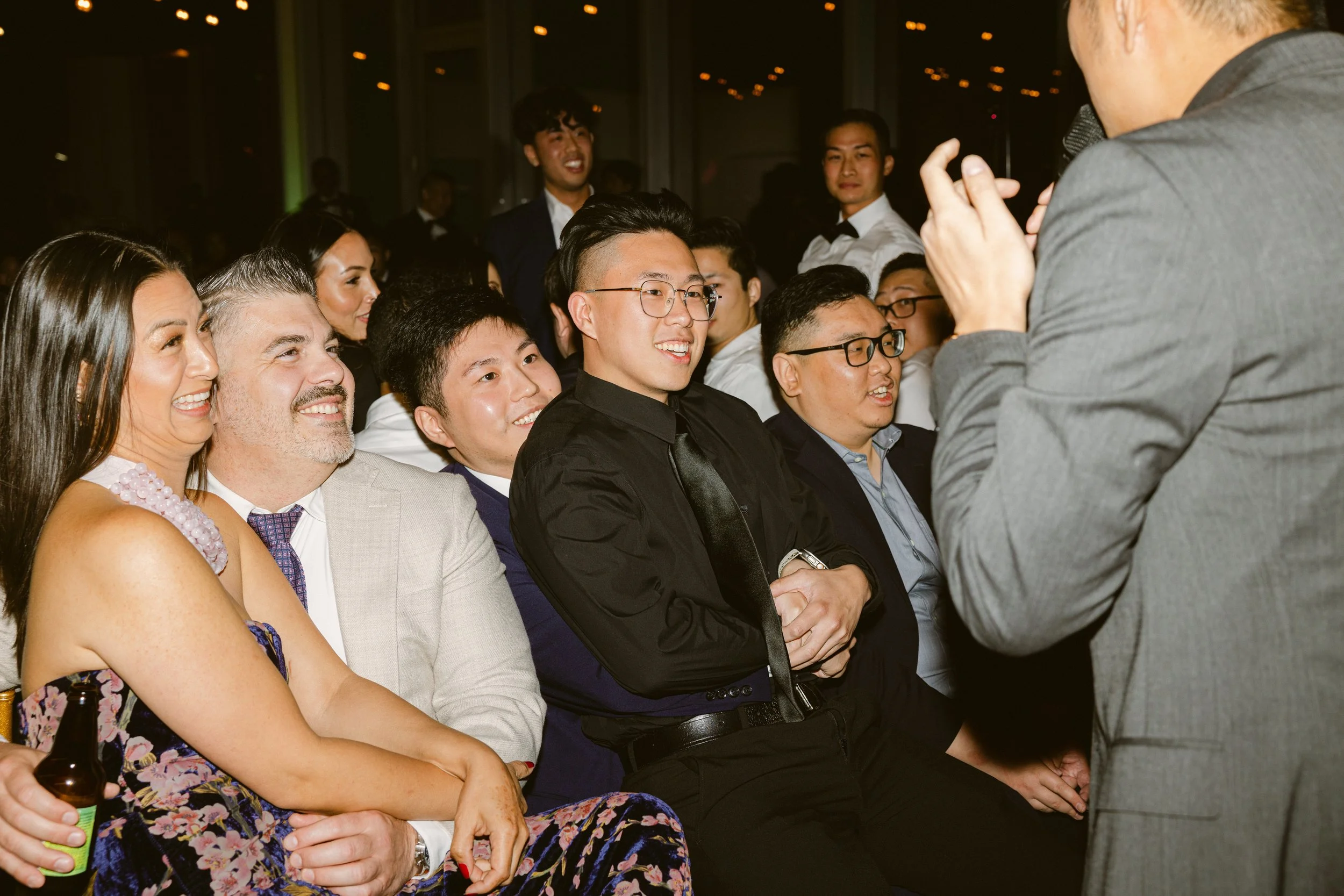 A group of people dressed in formal attire enjoying a performance or speech at an event or celebration.