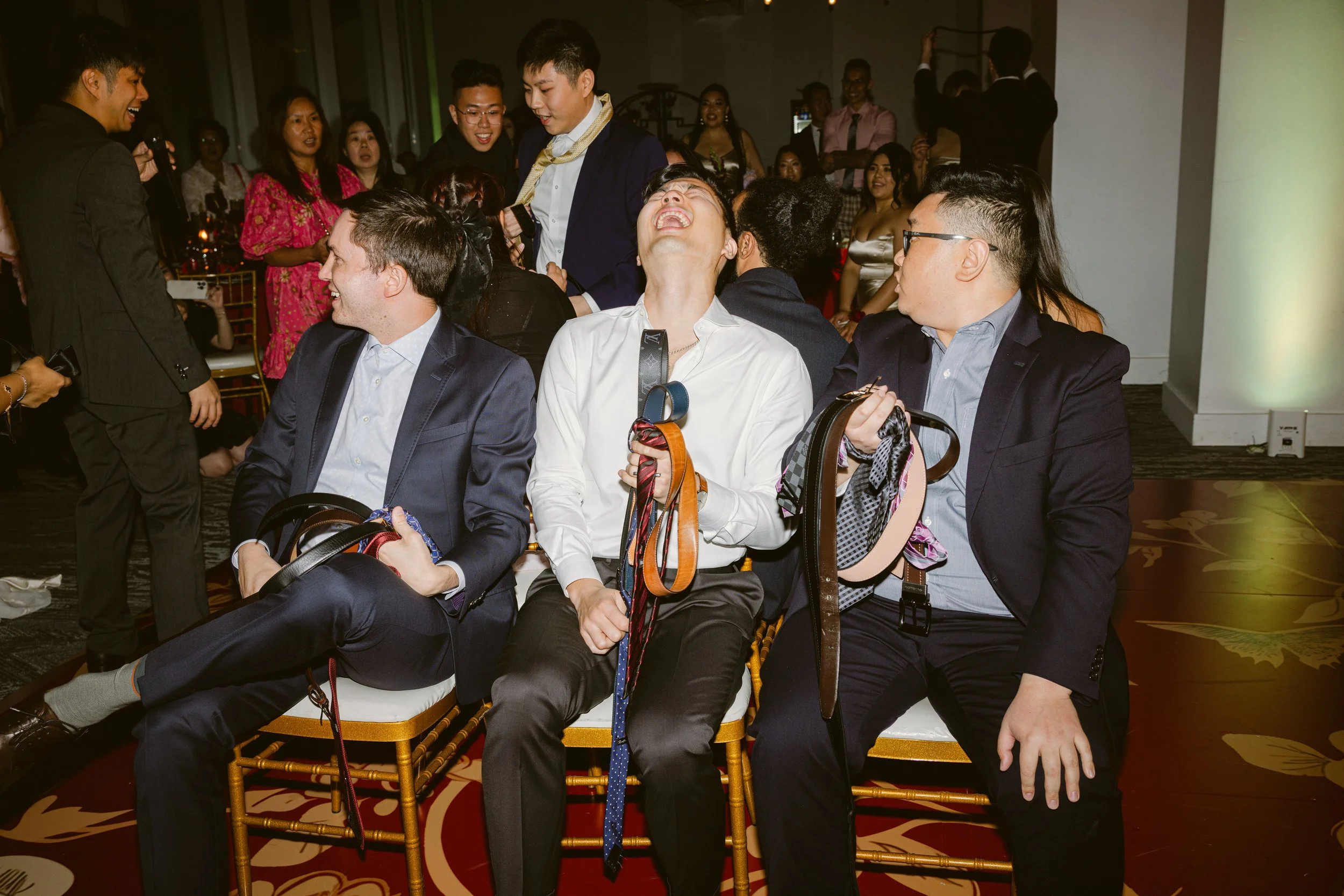 People at a social event, some laughing and talking, sitting and standing in a well-lit room.