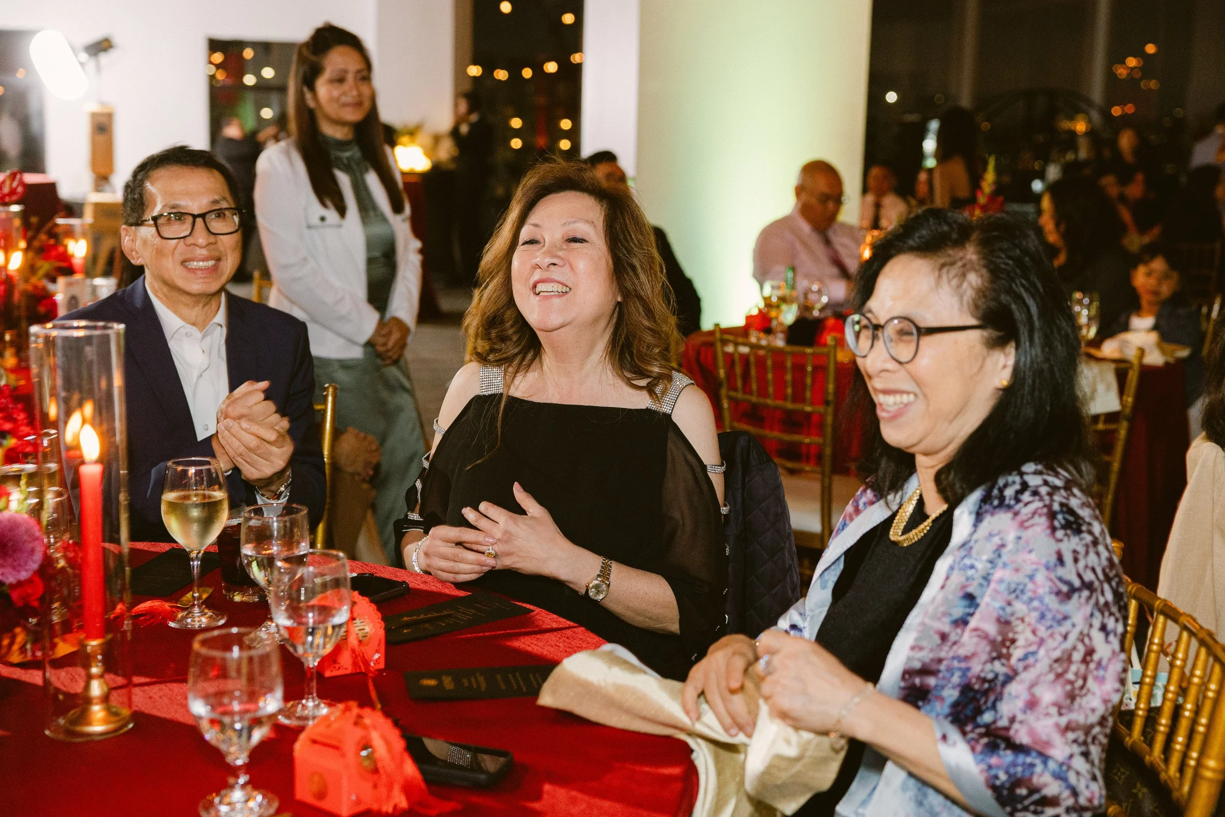 People enjoying themselves at a dinner party, sitting at a table decorated with flowers, candles, and glasses of wine, with a festive atmosphere and warm lighting.