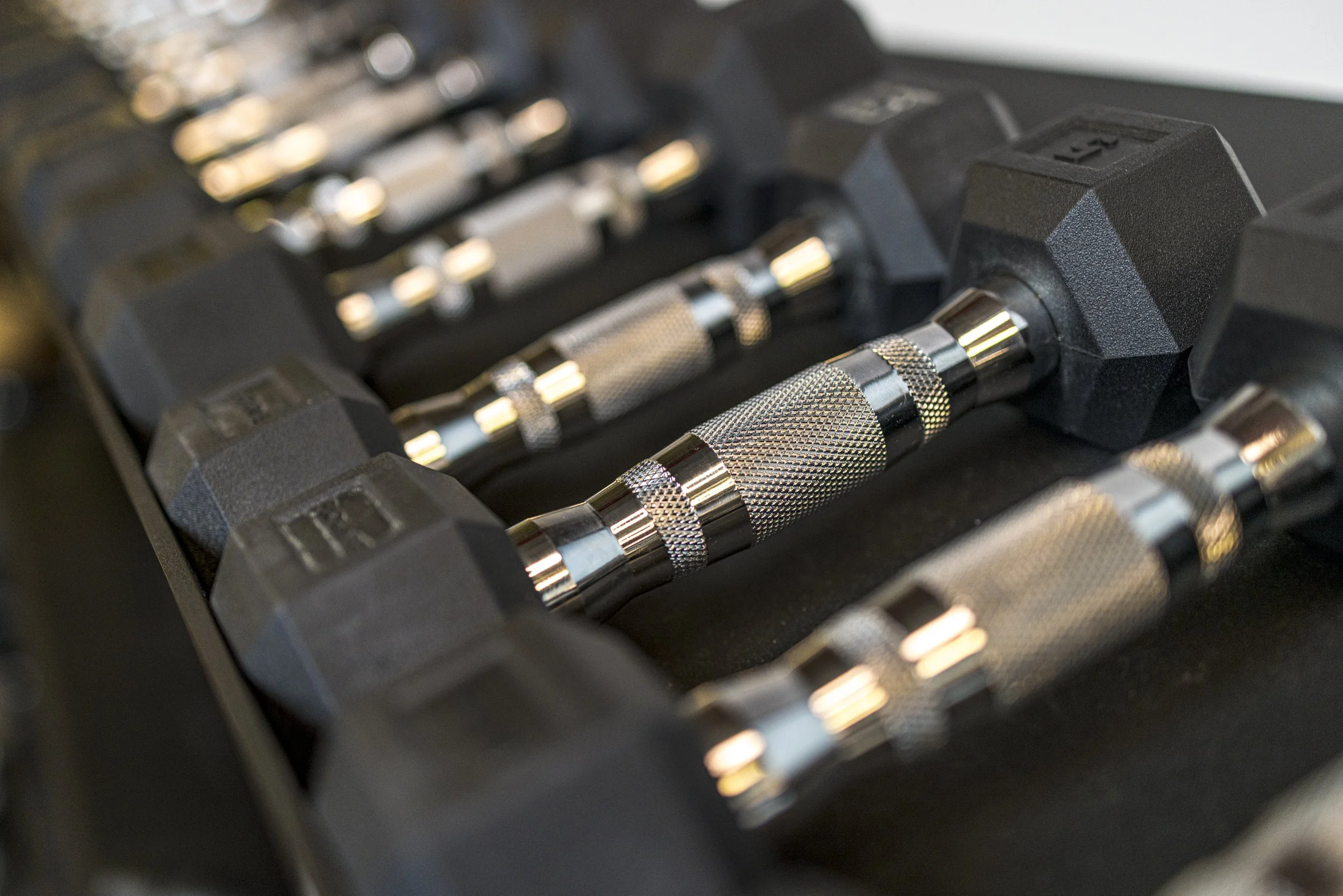 Close-up of multiple chrome-handled adjustable dumbbells in a black rack at FlySpace Physical Therapy in New York.