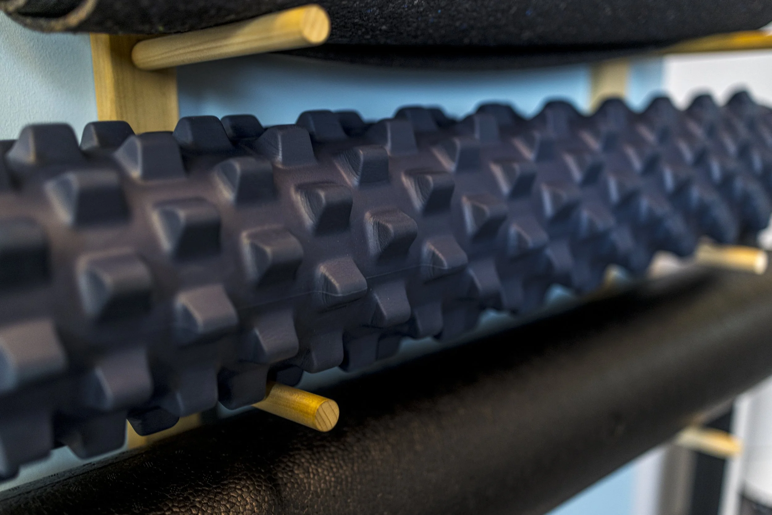 Close-up of a black rubber foam roller with textured surface, resting on a black surface with a wooden leg beneath.