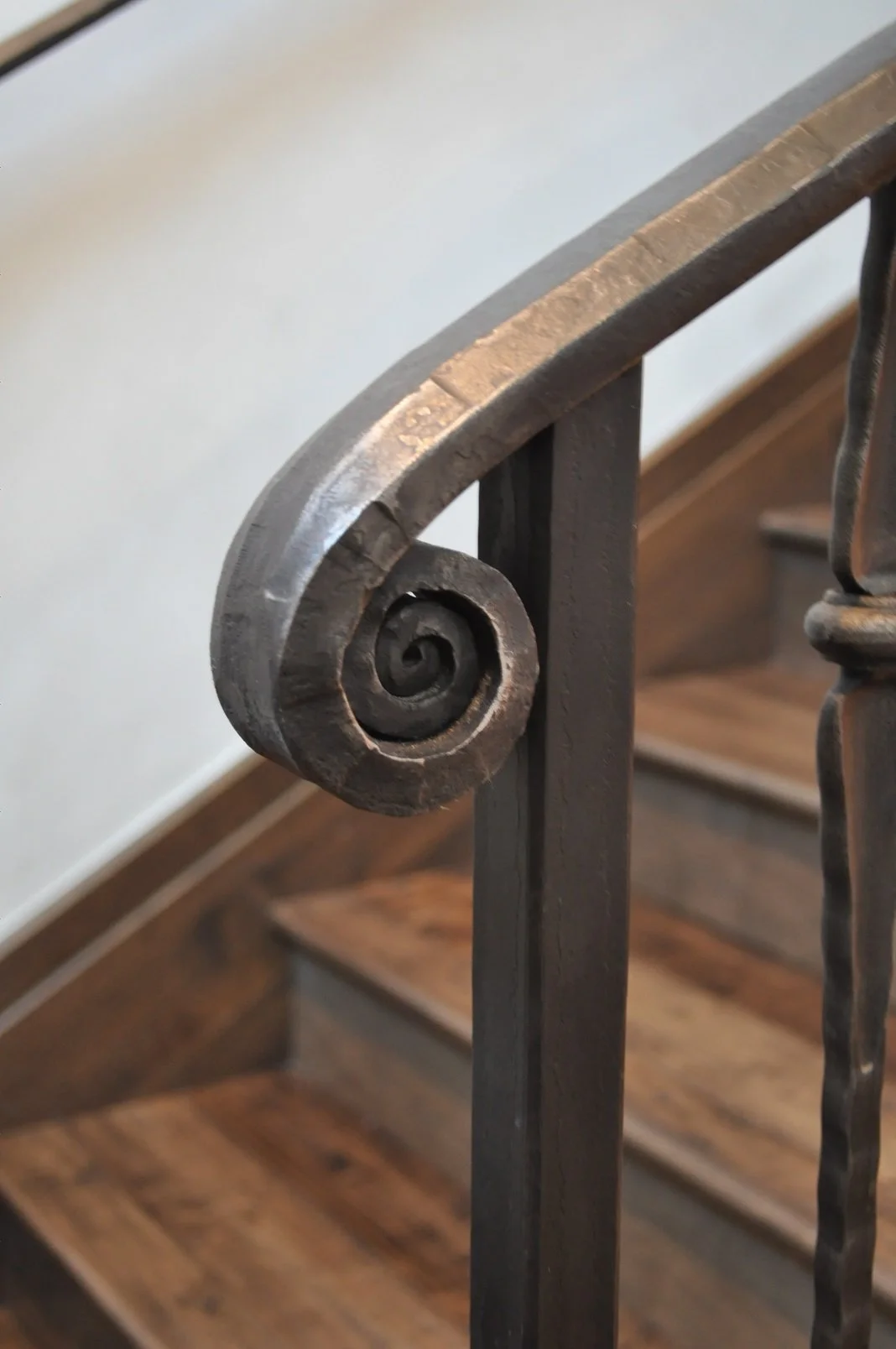 Close-up of a decorative spiral design on a black metal stair railing, with wooden stairs in the background.