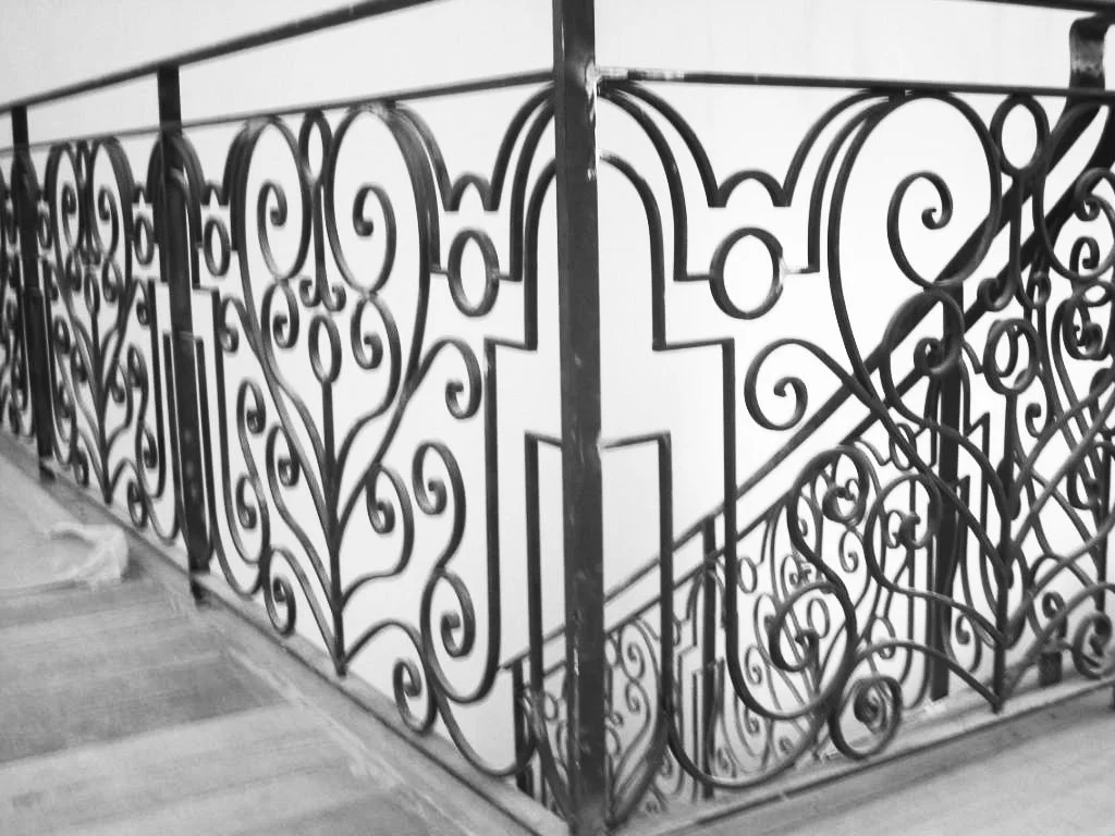 Black wrought iron decorative railing with intricate scrollwork on a staircase.