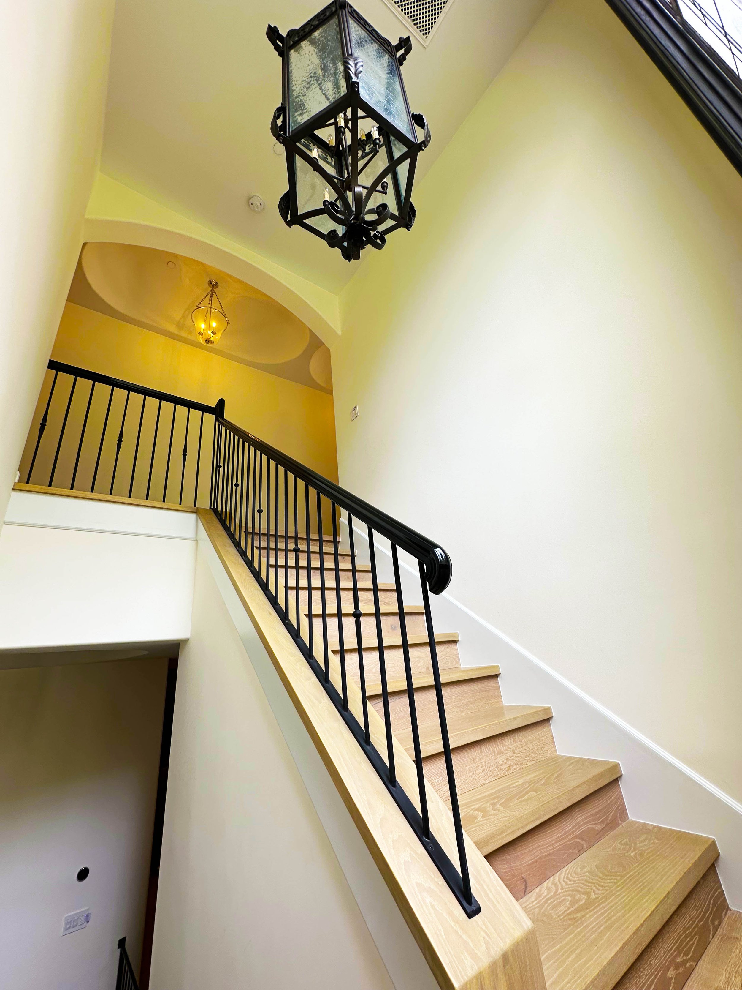 Photo of a staircase with wooden steps, black metal railing, yellow walls, skylight, and hanging light fixtures.