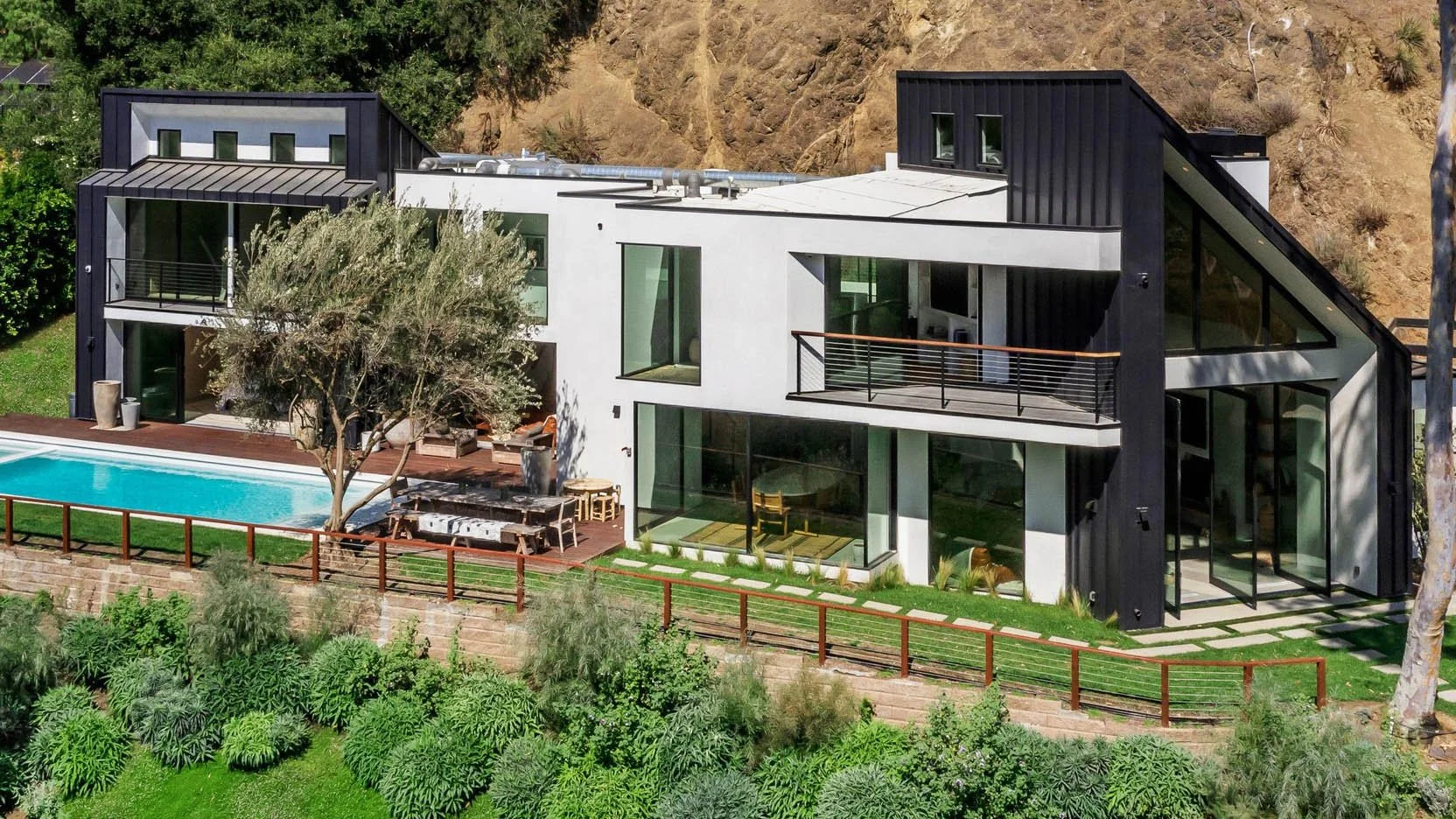 Modern multi-story house with large glass windows, black and white exterior, and a swimming pool in the backyard surrounded by greenery. stainless steel modern cable railings
