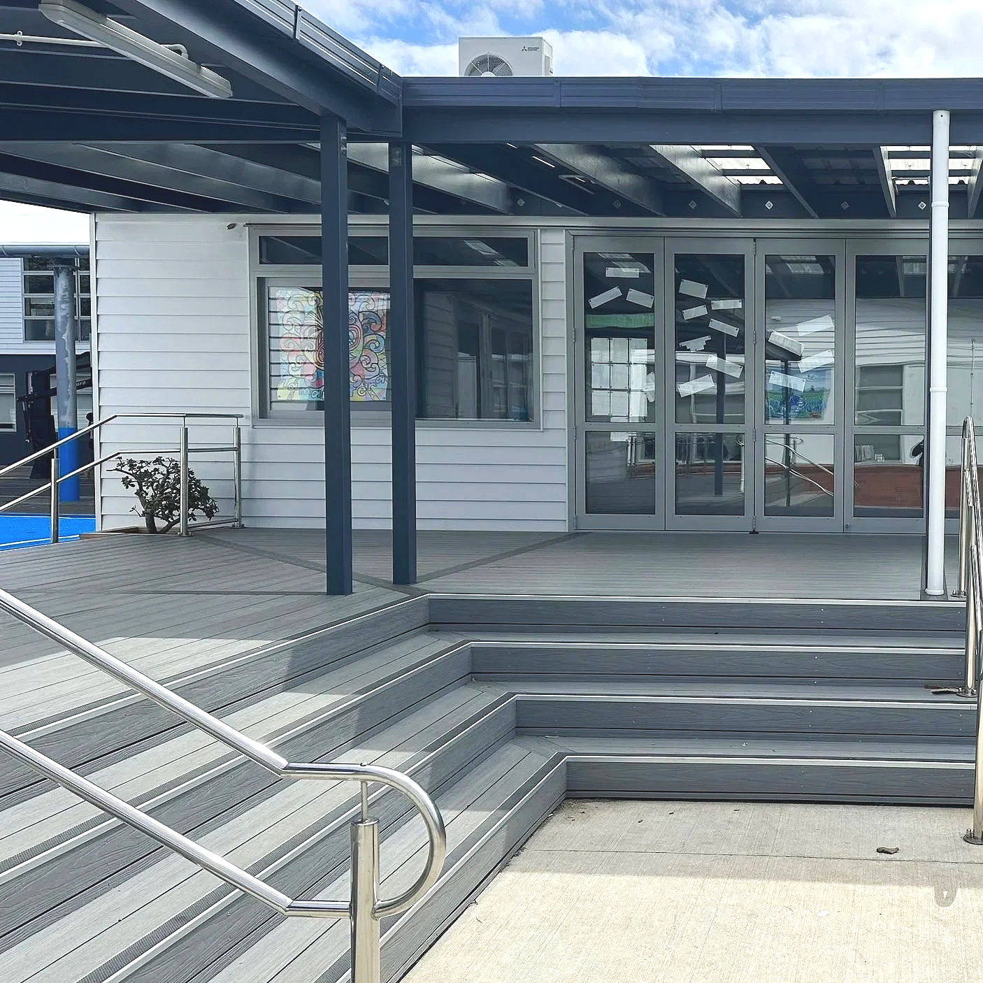 Exterior view of a Primary School building with a timber deck, ramp and stairs, glass doors, and large windows, with a cloudy sky above.
