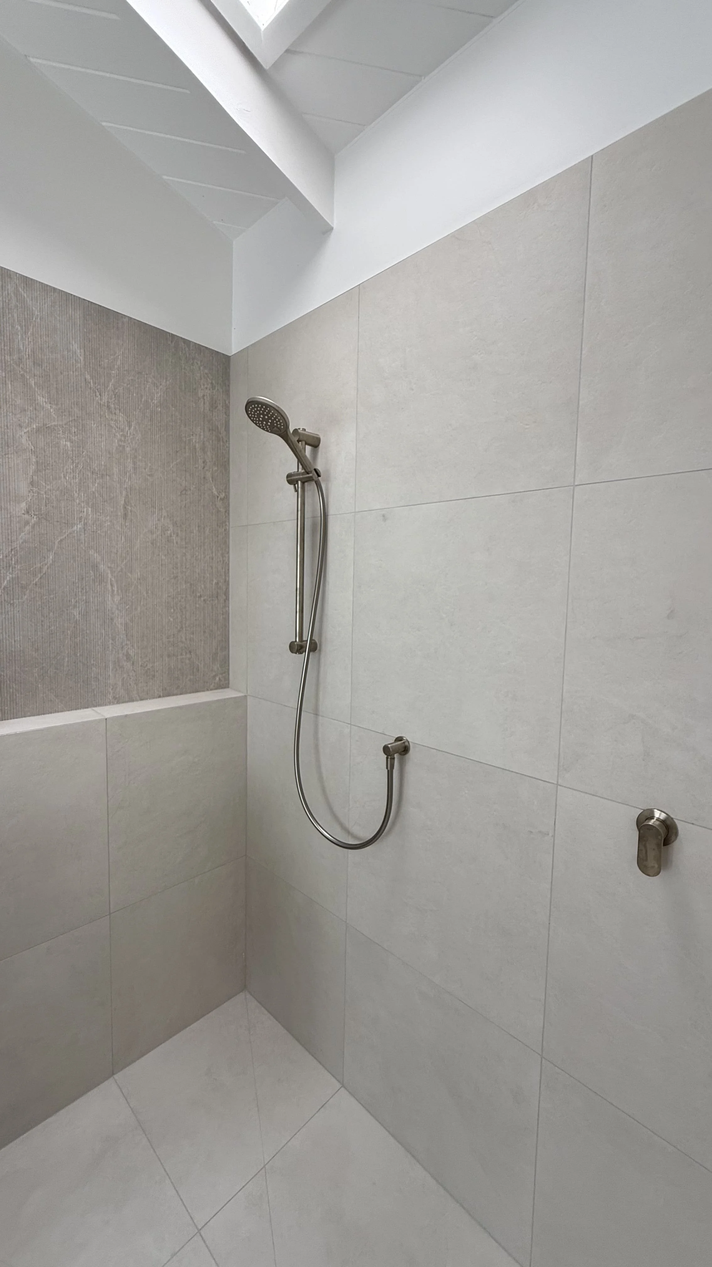 Large format wall tiles and feature wall tiles, along with a wall ledge and brushed nickel tapware creates a luxurious bathroom experience