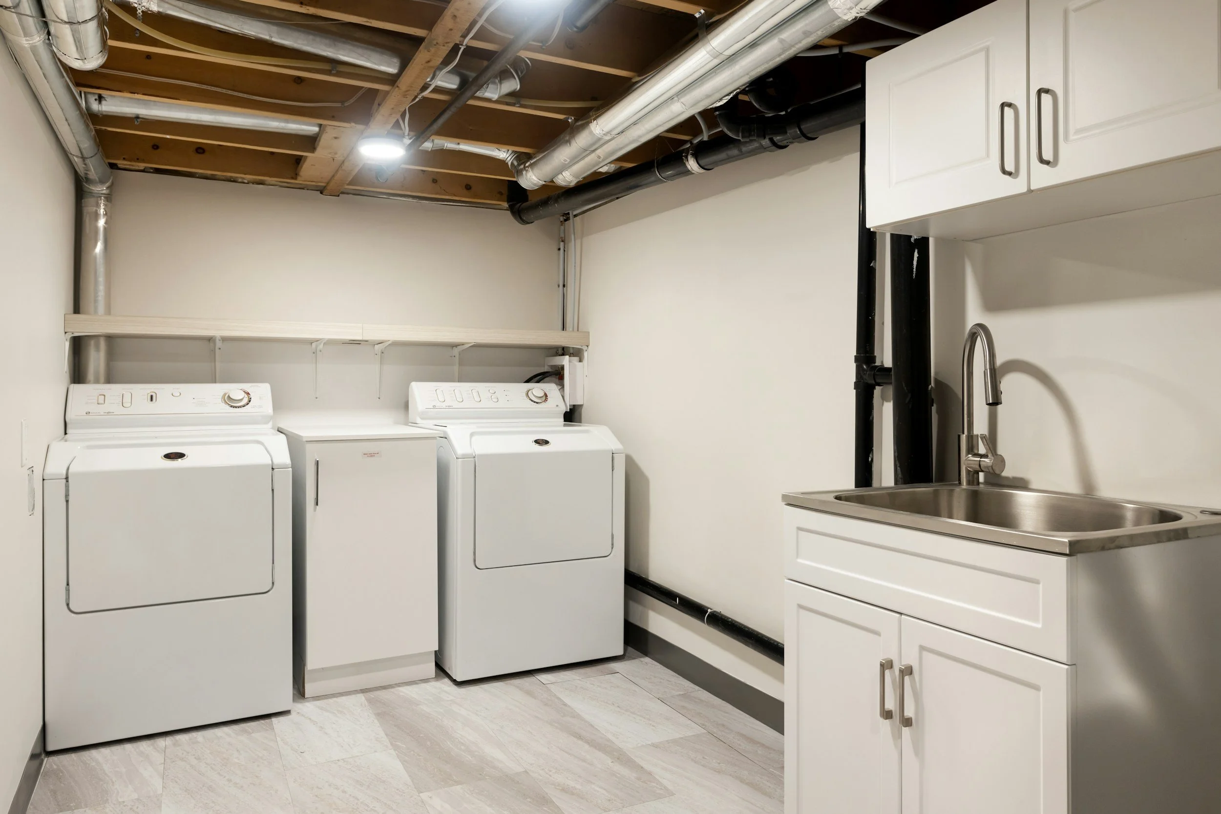 laundry room with washer and dryer, utility sink, white cabinets, and exposed ceiling pipes