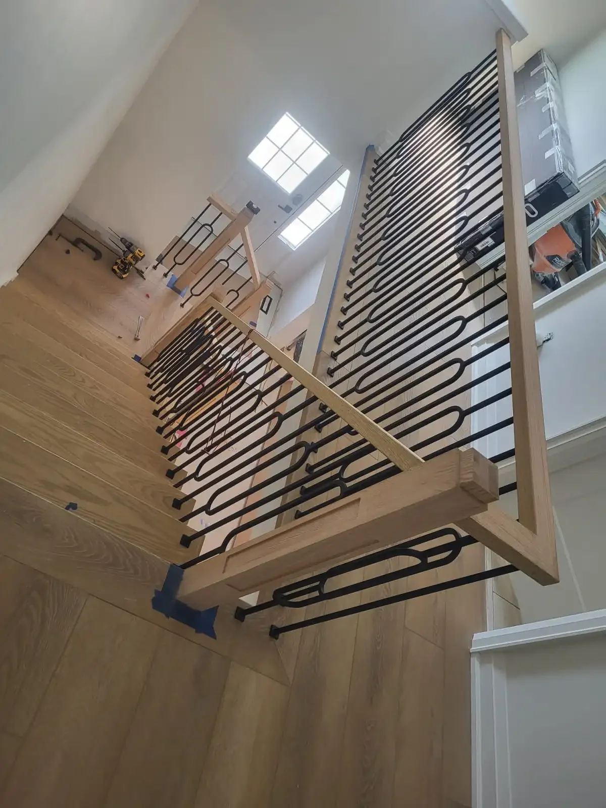 Addison's stair railing under construction with black metal balusters and unfinished wooden handrails and posts in a house interior.