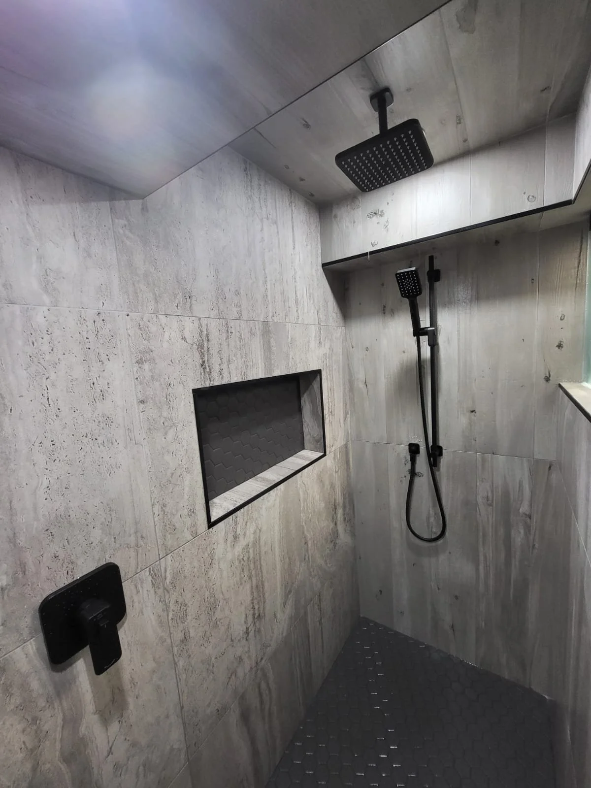 Modern shower with black rain and handheld showerheads, beige tile walls, built-in niche, and black fixtures.