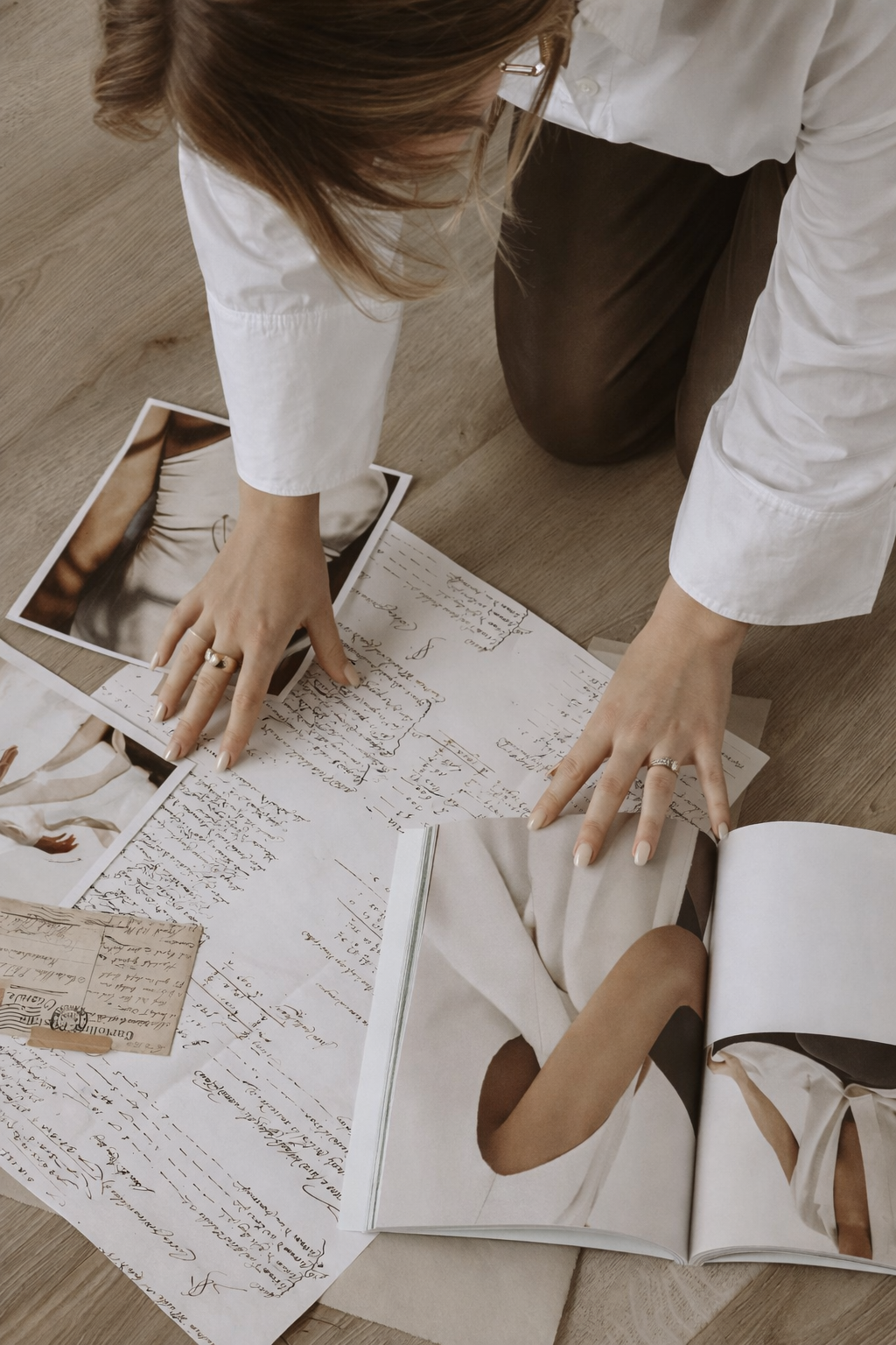 Person organizing fashion magazine pages and handwritten notes on the floor.