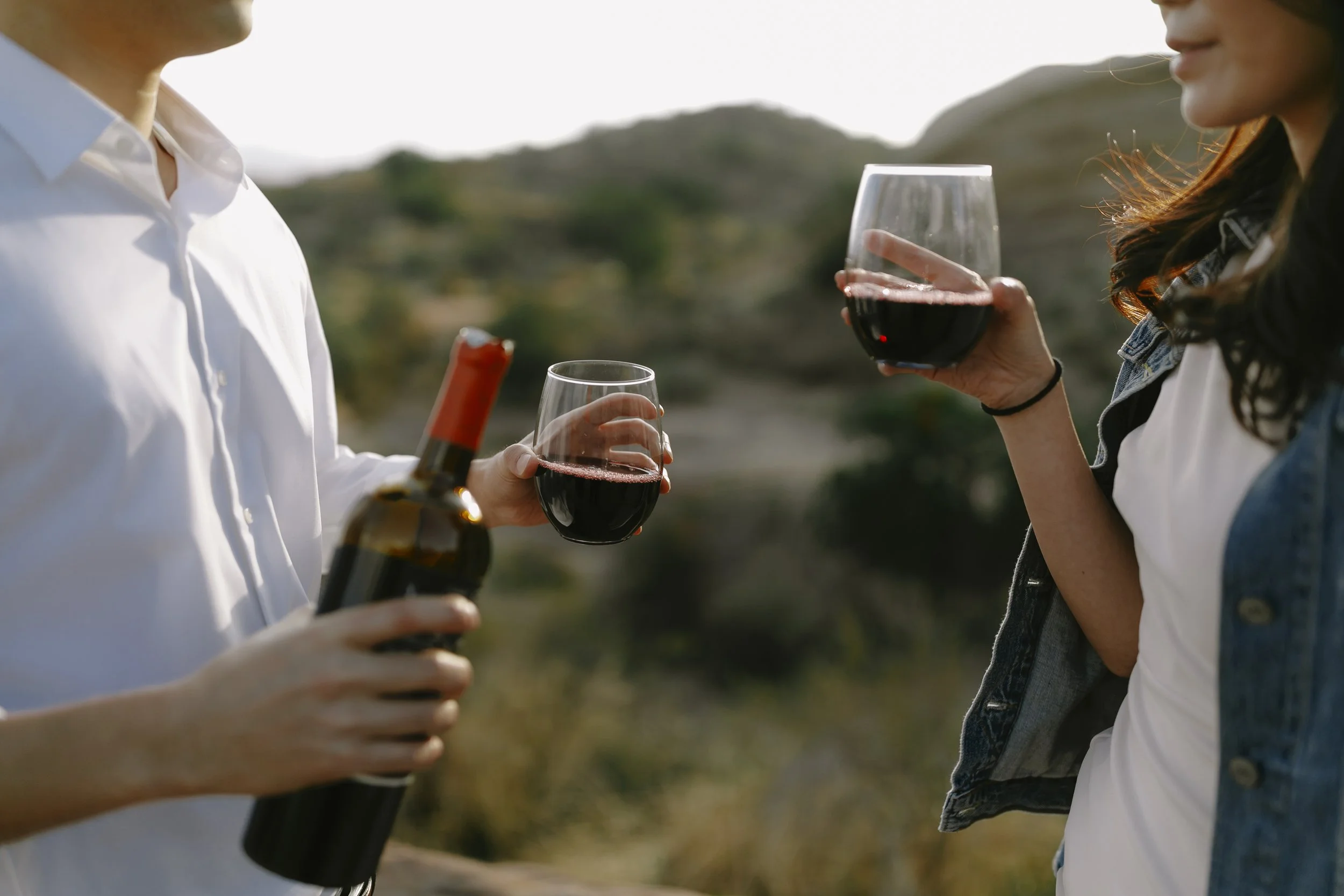 A couple sharing red wine outdoors during their engagement session.