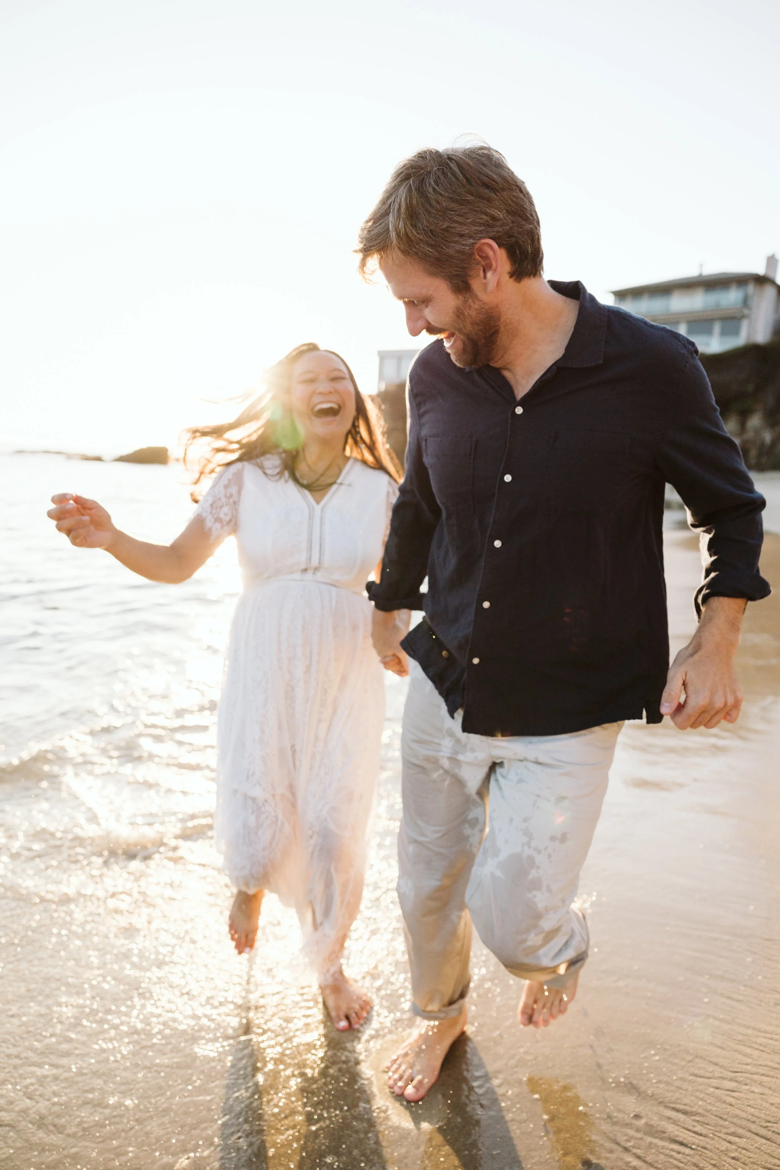 Couple holding hands and splashing through the surf during a sunlit beach photoshoot.