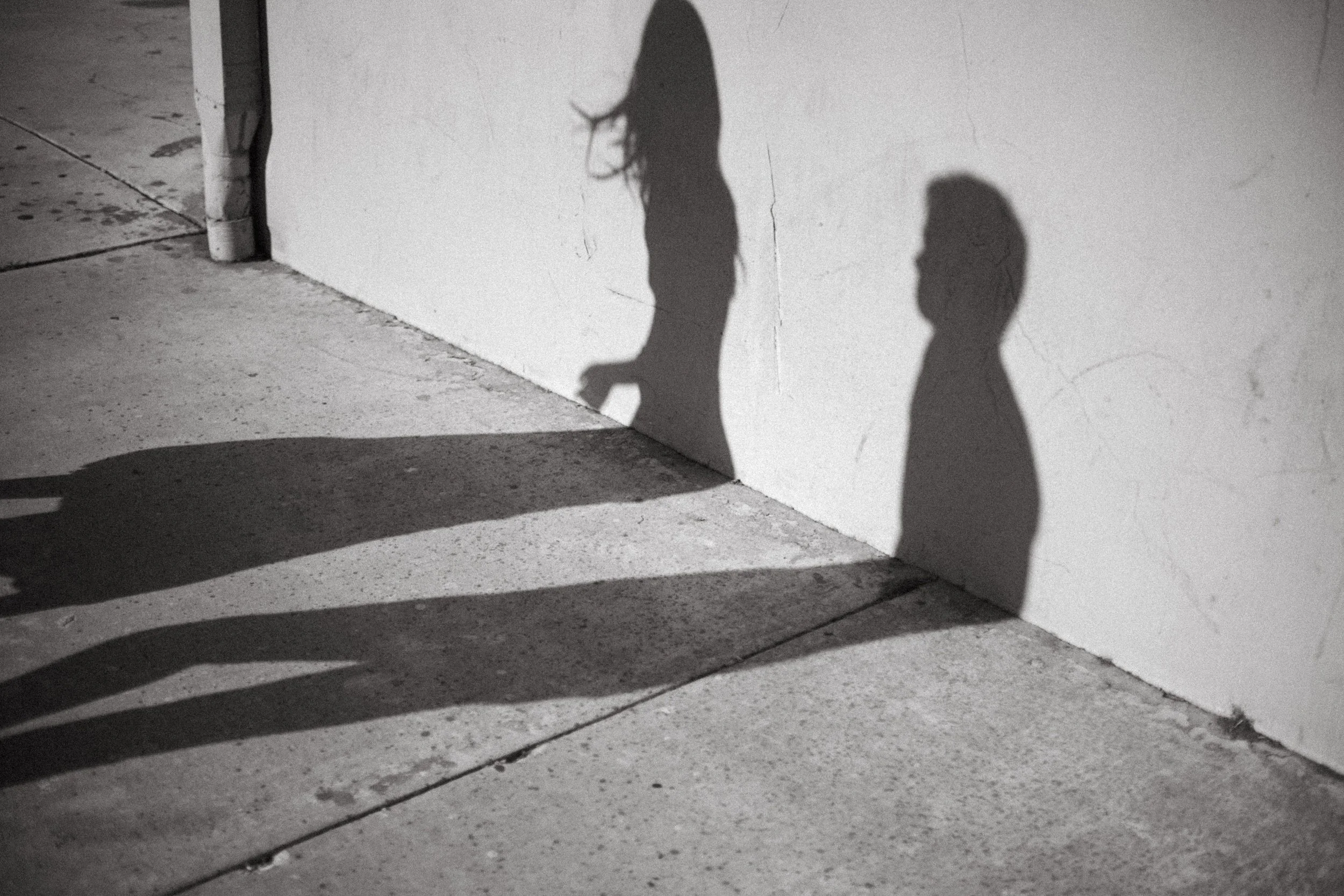 Black and white photograph of a couple’s shadows falling across a sunlit wall and pavement.