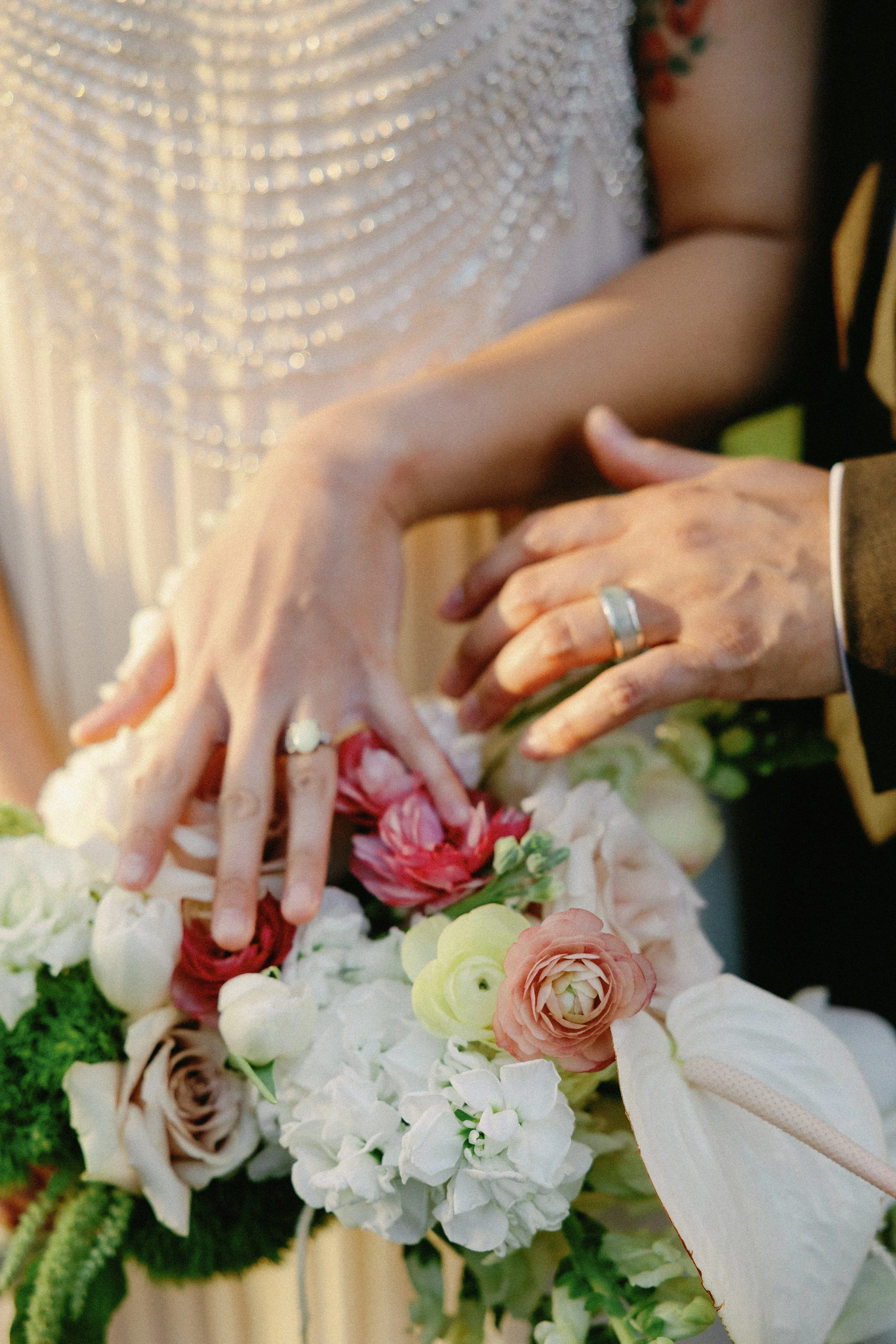 Close-up of a bride holding a bouquet of white and blush flowers against her beaded wedding dress.