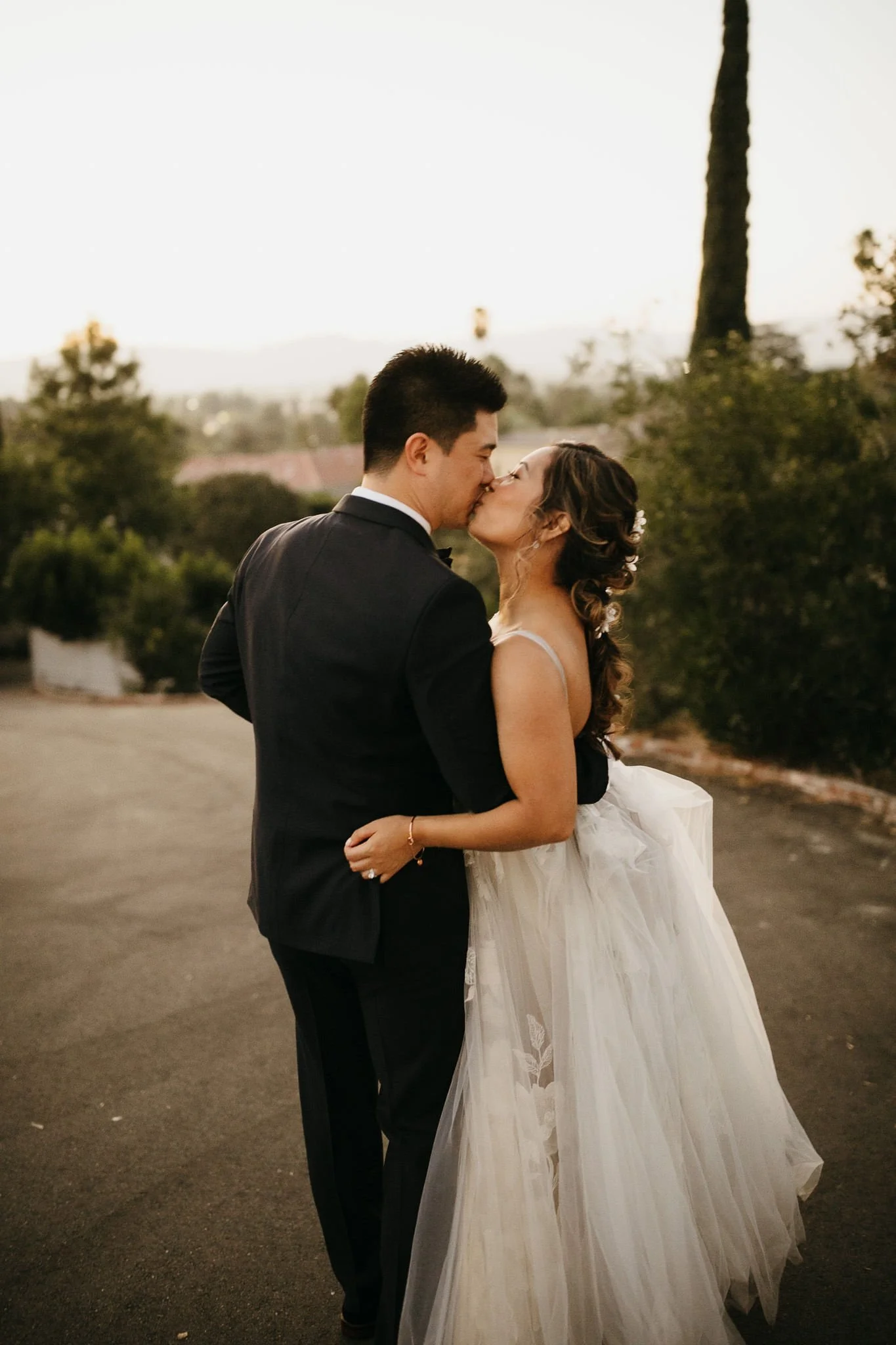 Bride and groom kissing on a garden path, with the bride holding her tulle skirt.