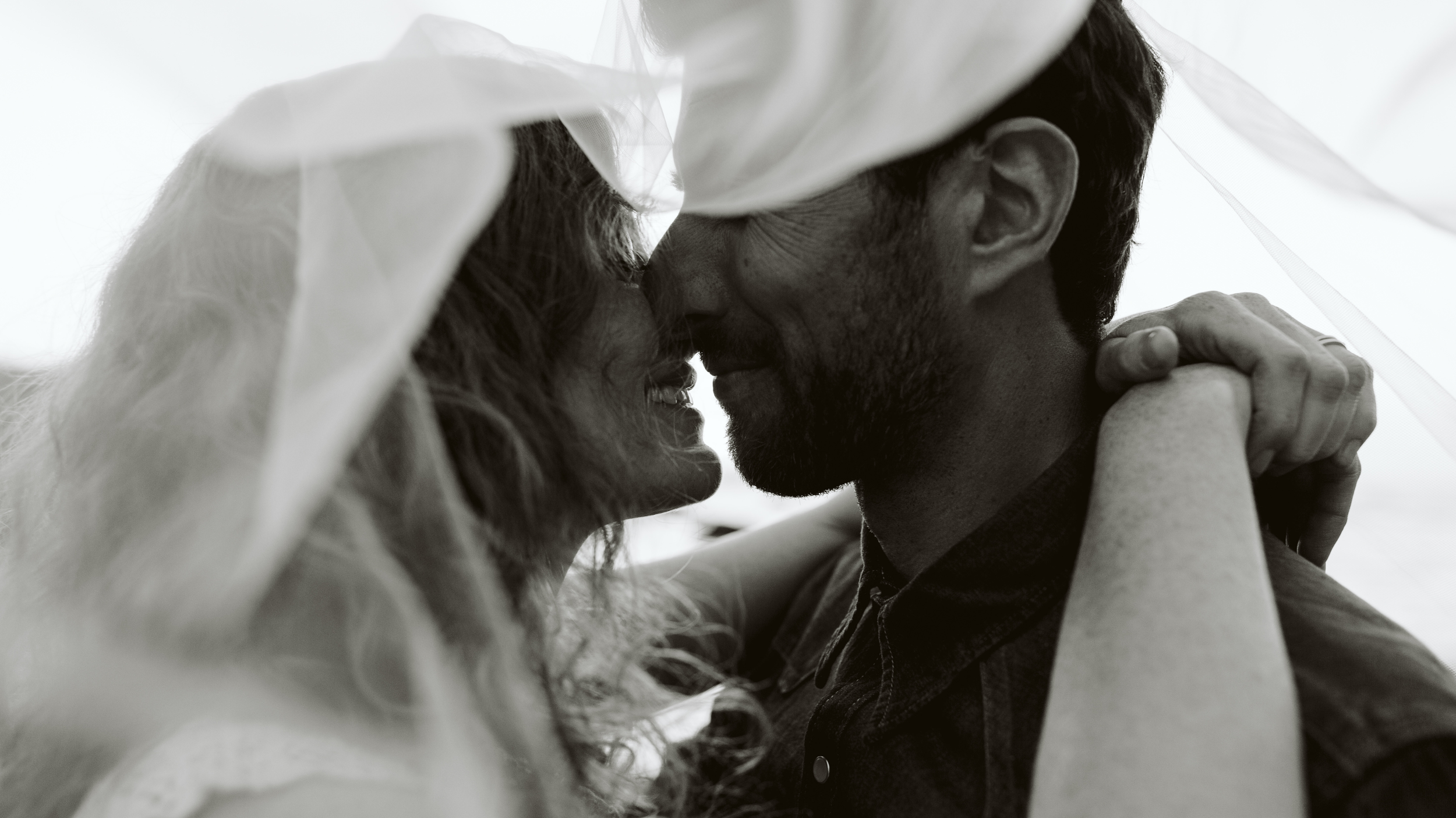 Wedding couple touching foreheads beneath the bride’s veil.