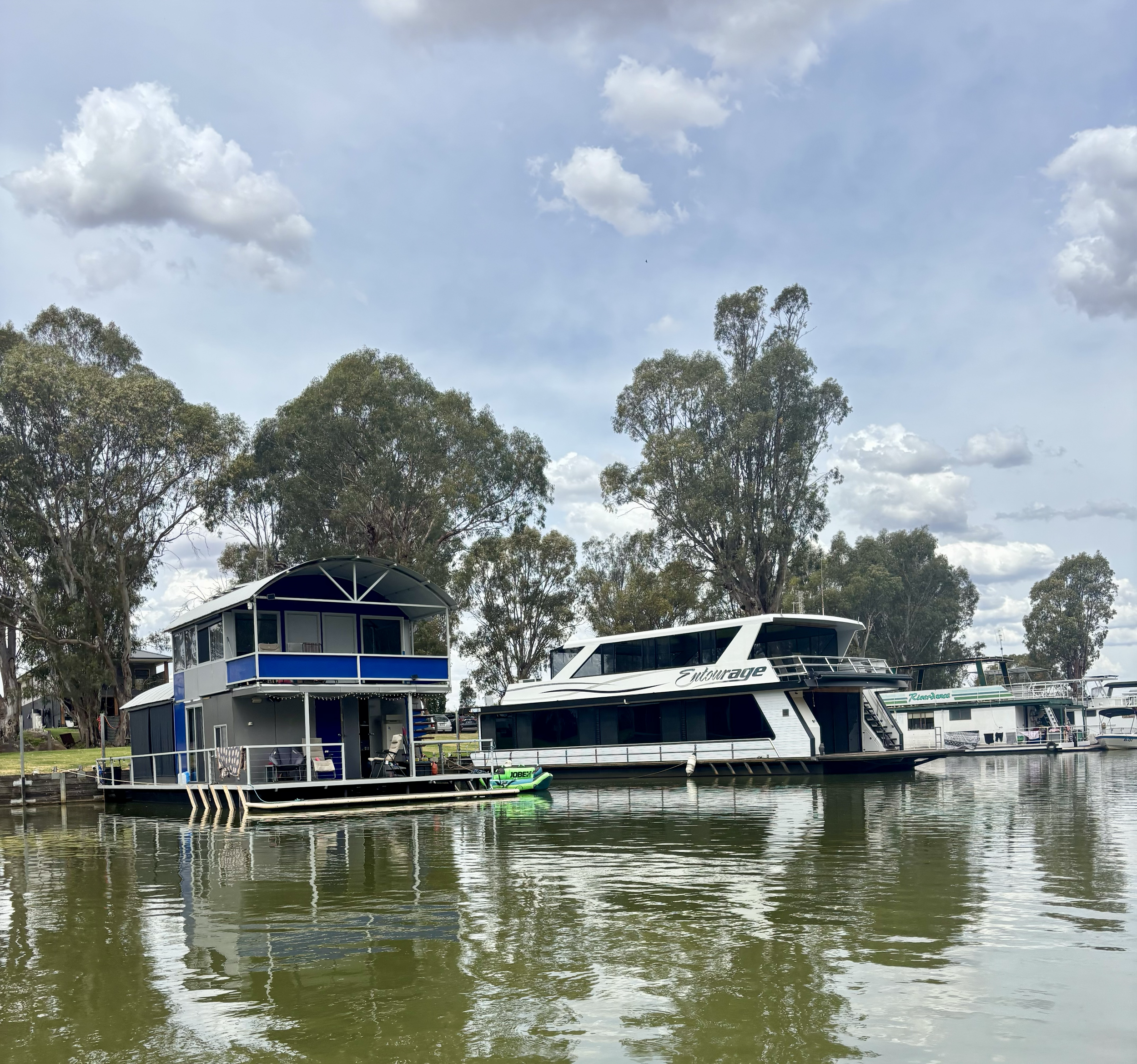Two boats docked on a river with trees and a partly cloudy sky in the background.