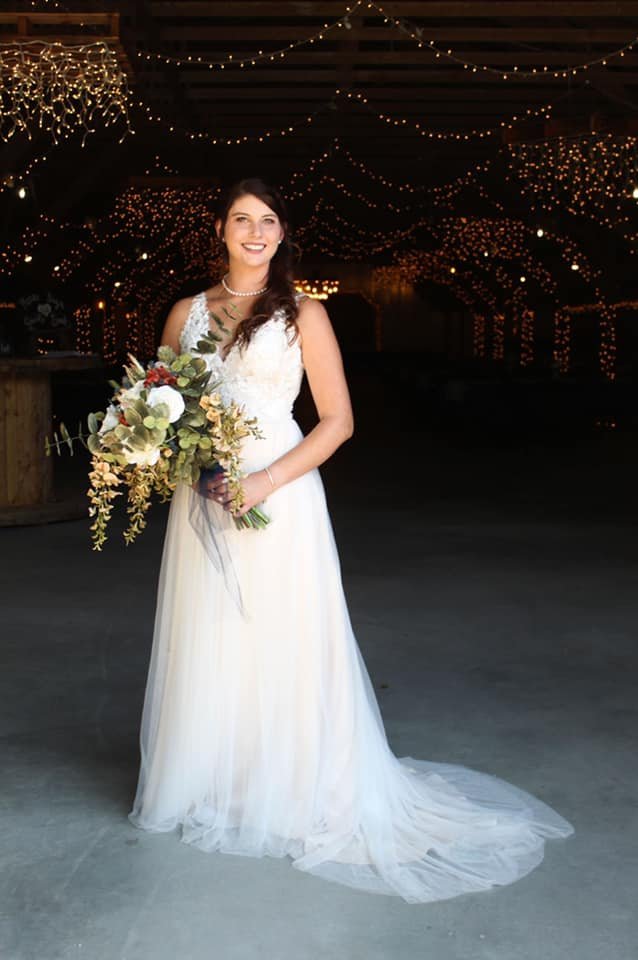 A bride in a white wedding dress holding a bouquet of flowers, standing under string lights at night.