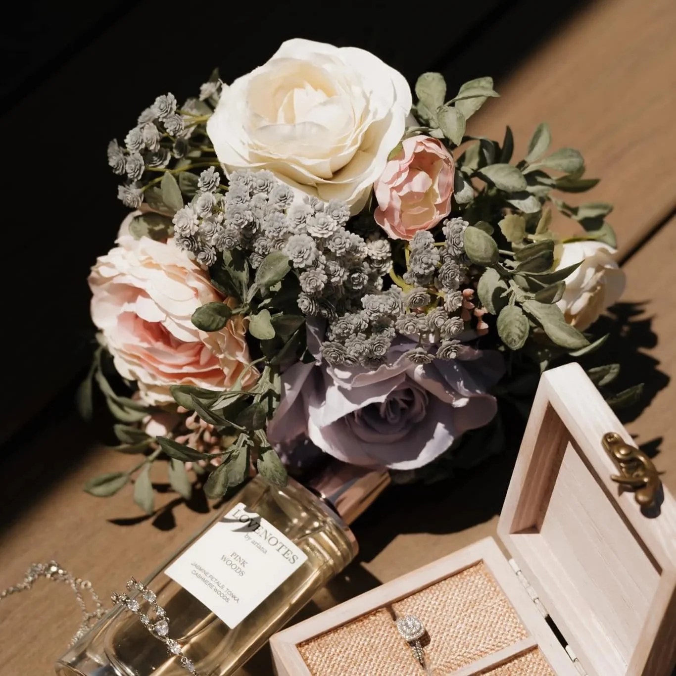 A bouquet of pink and white flowers, a jewelry box with a ring inside, and a perfume bottle labeled 'LOVE NOTES' on a wooden surface.