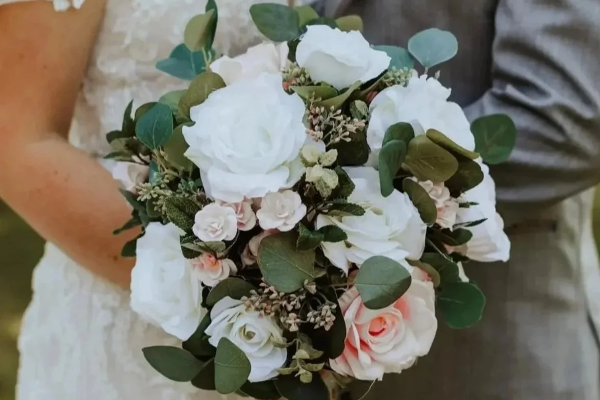 Close-up of a bride holding a bouquet of white roses, small pink roses, eucalyptus leaves, and other greenery.